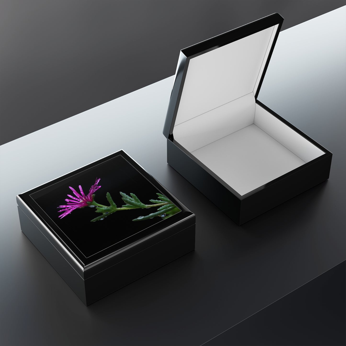Black jewelry box with a pink flower and green leaves on a reflective surface