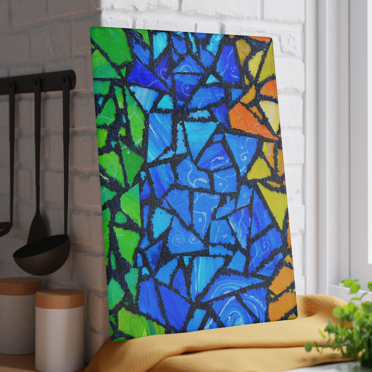 Colorful mosaic art piece on a white brick wall with kitchen utensils in the background.