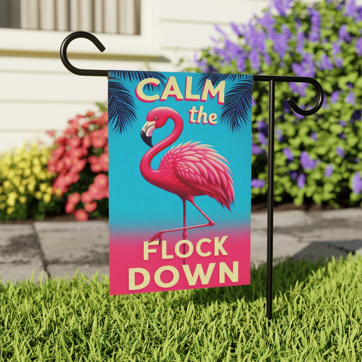 Garden flag with flamingo design and text 'Calm the Flock Down' on a grassy lawn.