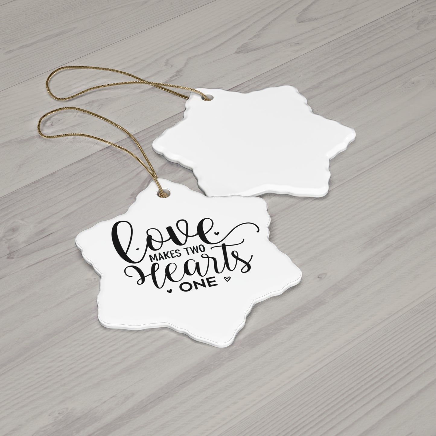Two white heart-shaped tags with 'Love makes two hearts one' text on a wooden surface.