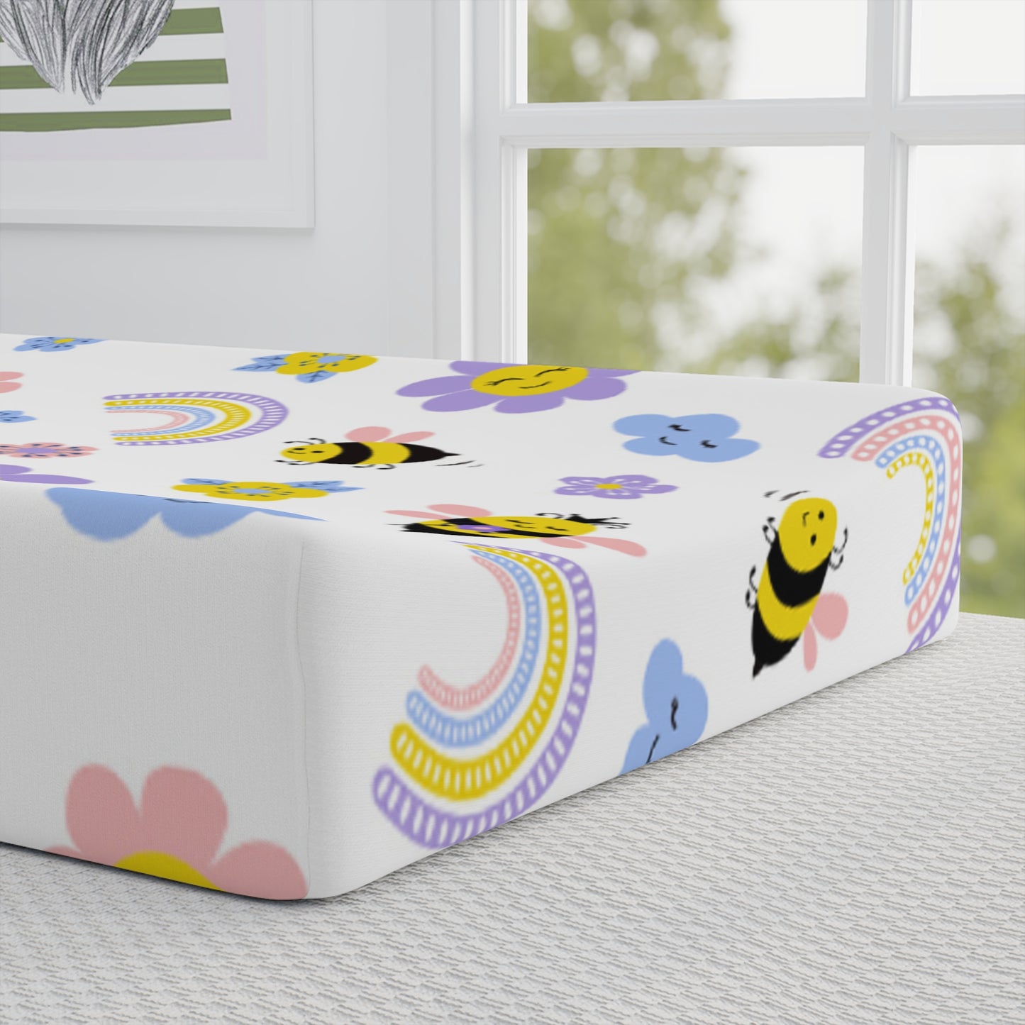 Fitted sheet with bee and rainbow pattern on a bed in a room with a window.