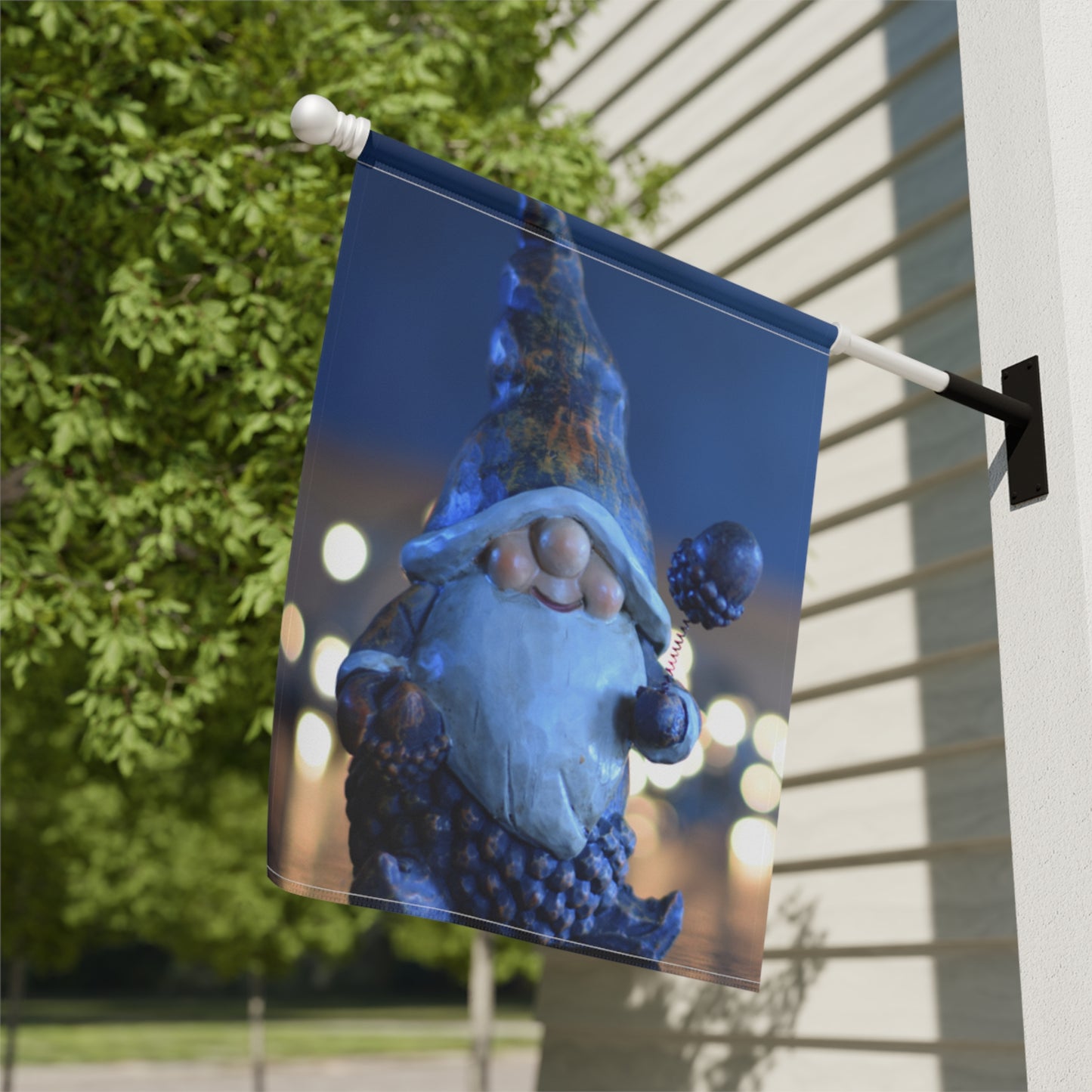 Decorative garden flag with a gnome design on a pole against a building and tree background.