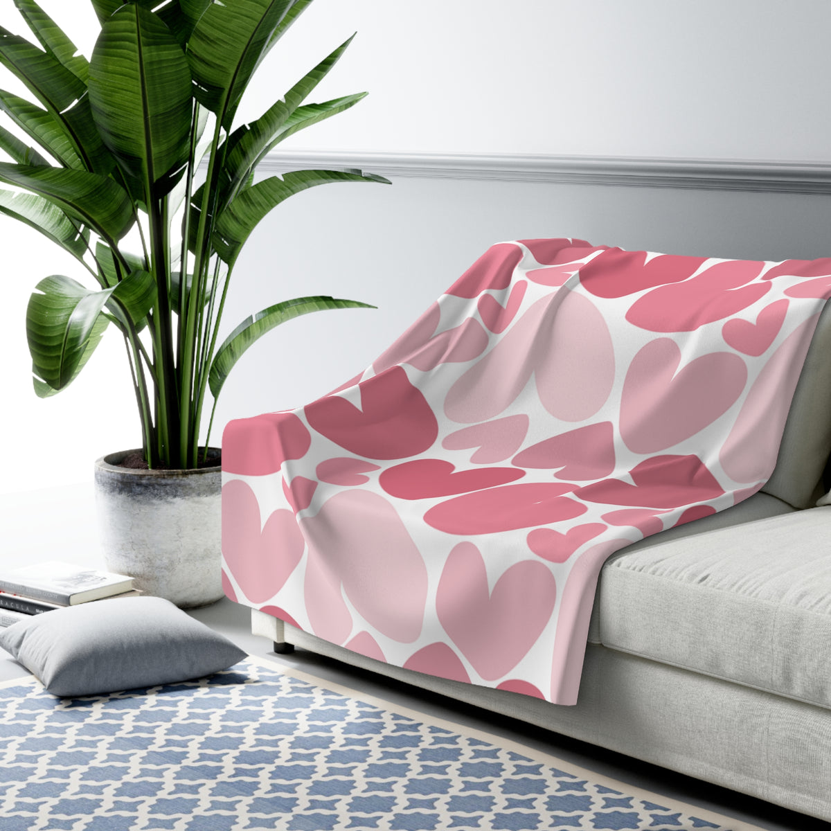 Pink floral patterned blanket on a gray sofa with a plant and rug in the background