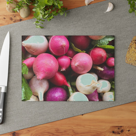 Assorted radishes on a gray surface with a knife and greenery in the background.