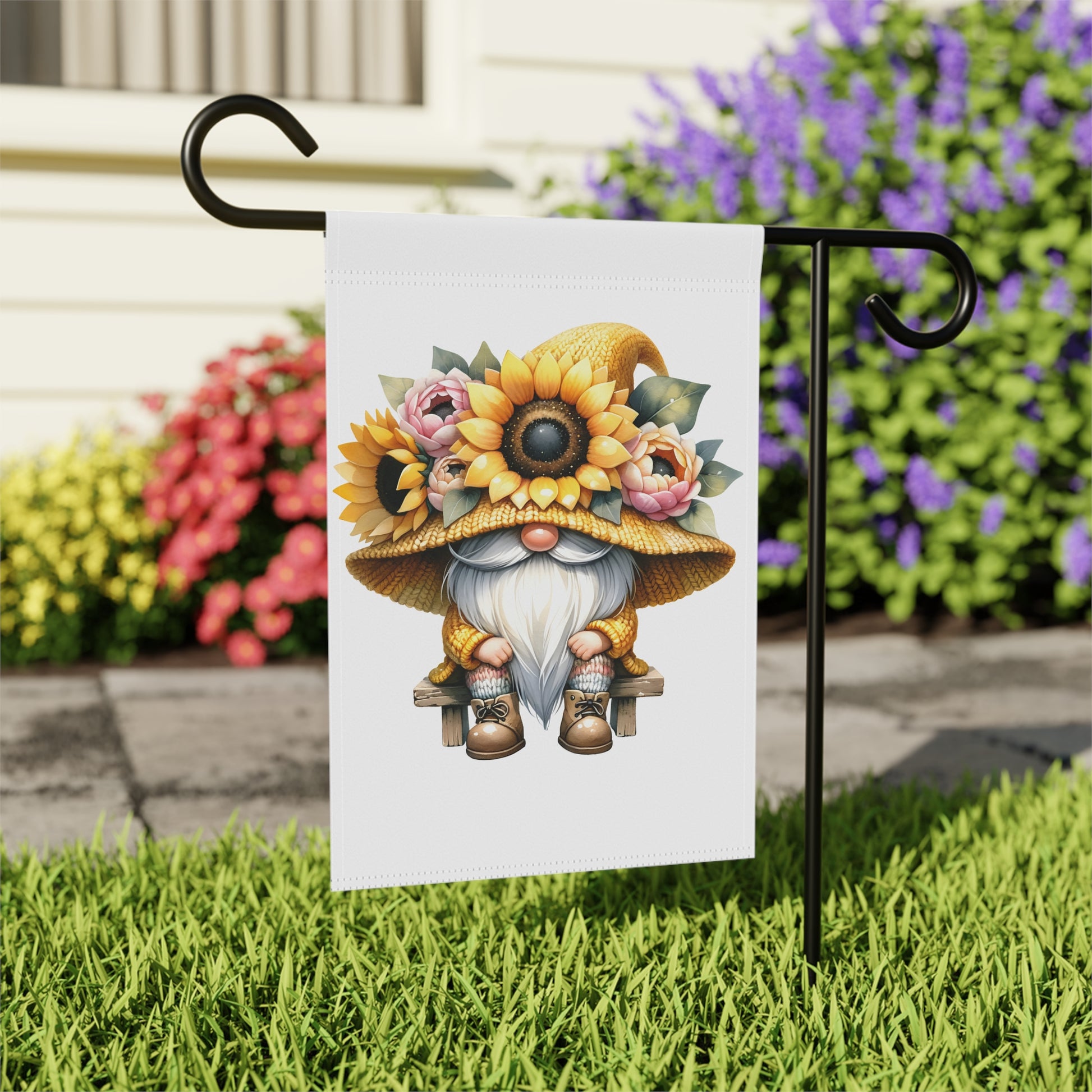 Garden flag with a gnome design featuring sunflowers and flowers, attached to a stand outdoors.