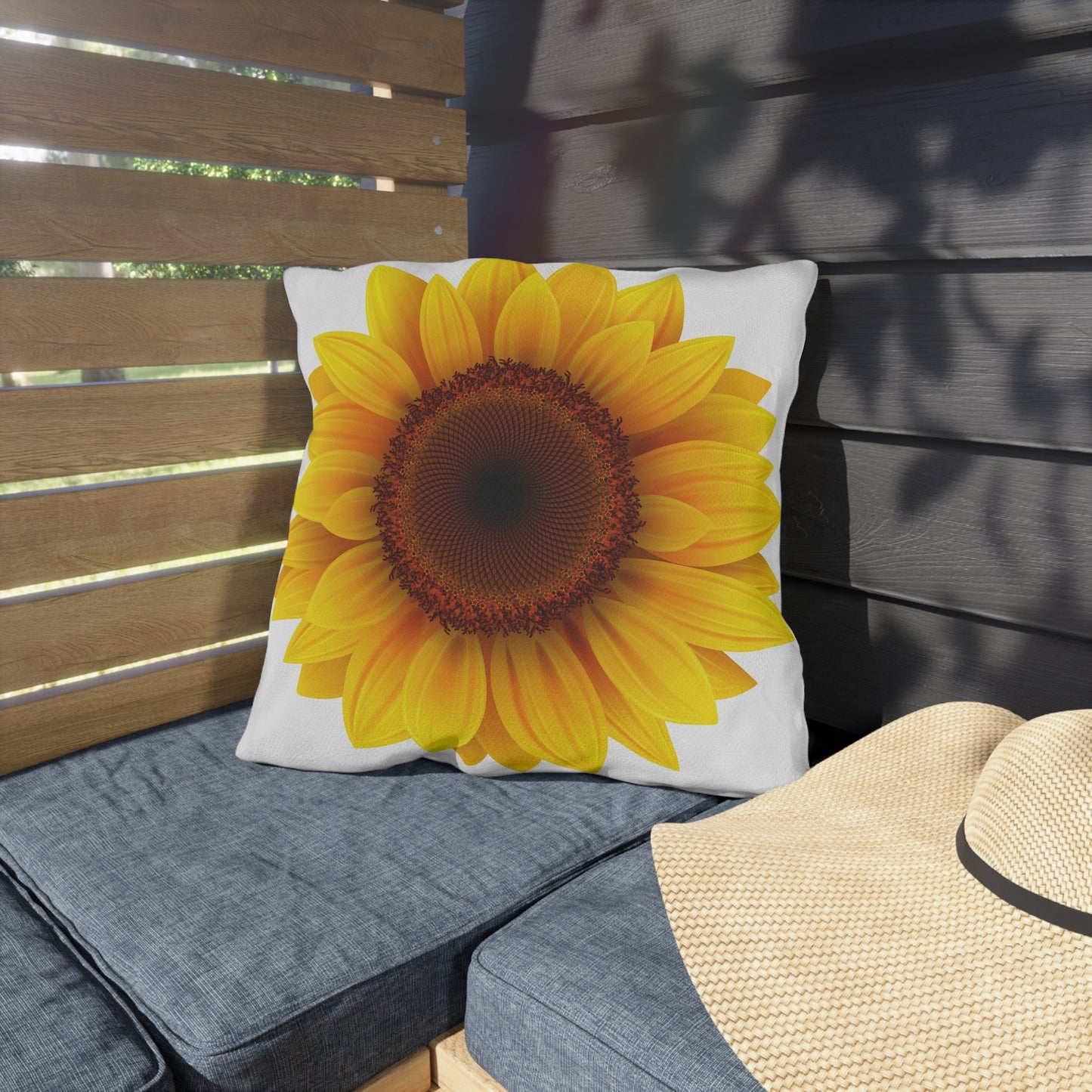 Sunflower pillow on a gray cushion with a wooden bench and straw hat in the background