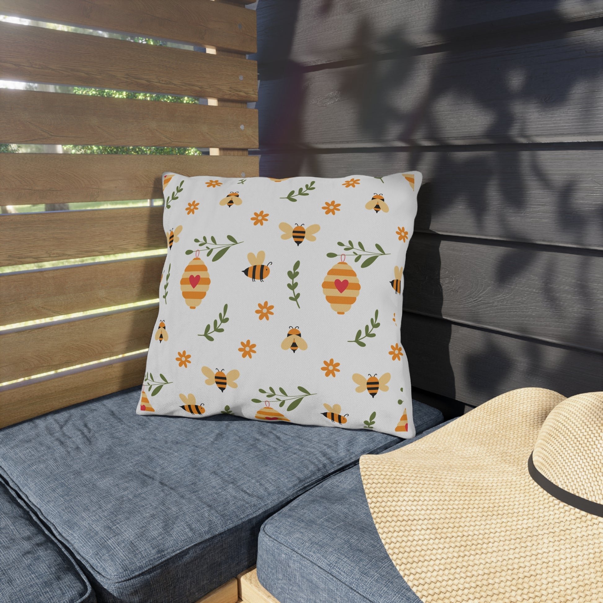 Decorative pillow with bee and lantern pattern on a gray cushioned bench.