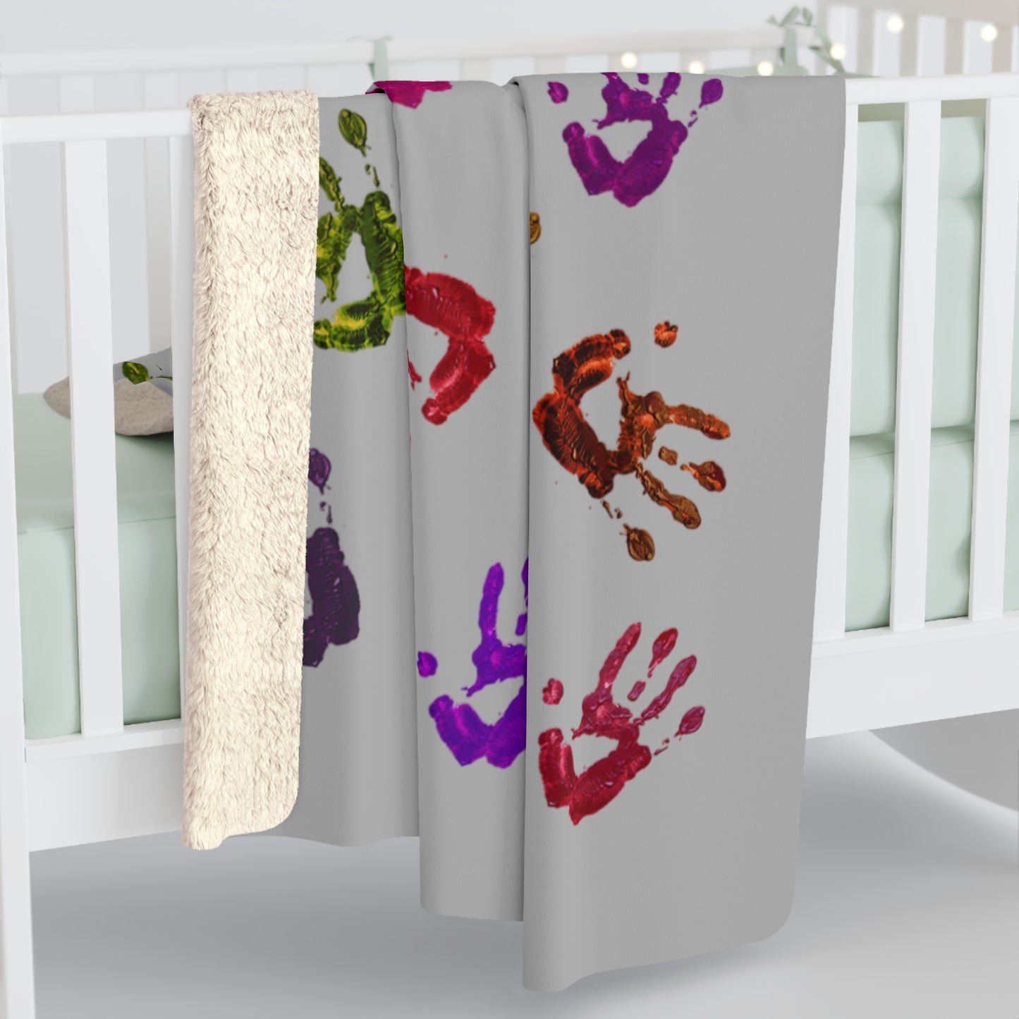 Gray blanket with colorful handprints in a crib setting