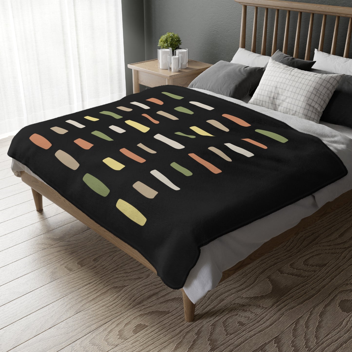 Bed with a black blanket featuring colorful abstract pattern in a bedroom setting.