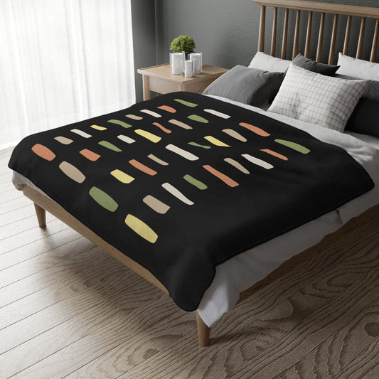 Bed with a black blanket featuring colorful abstract pattern in a bedroom setting.