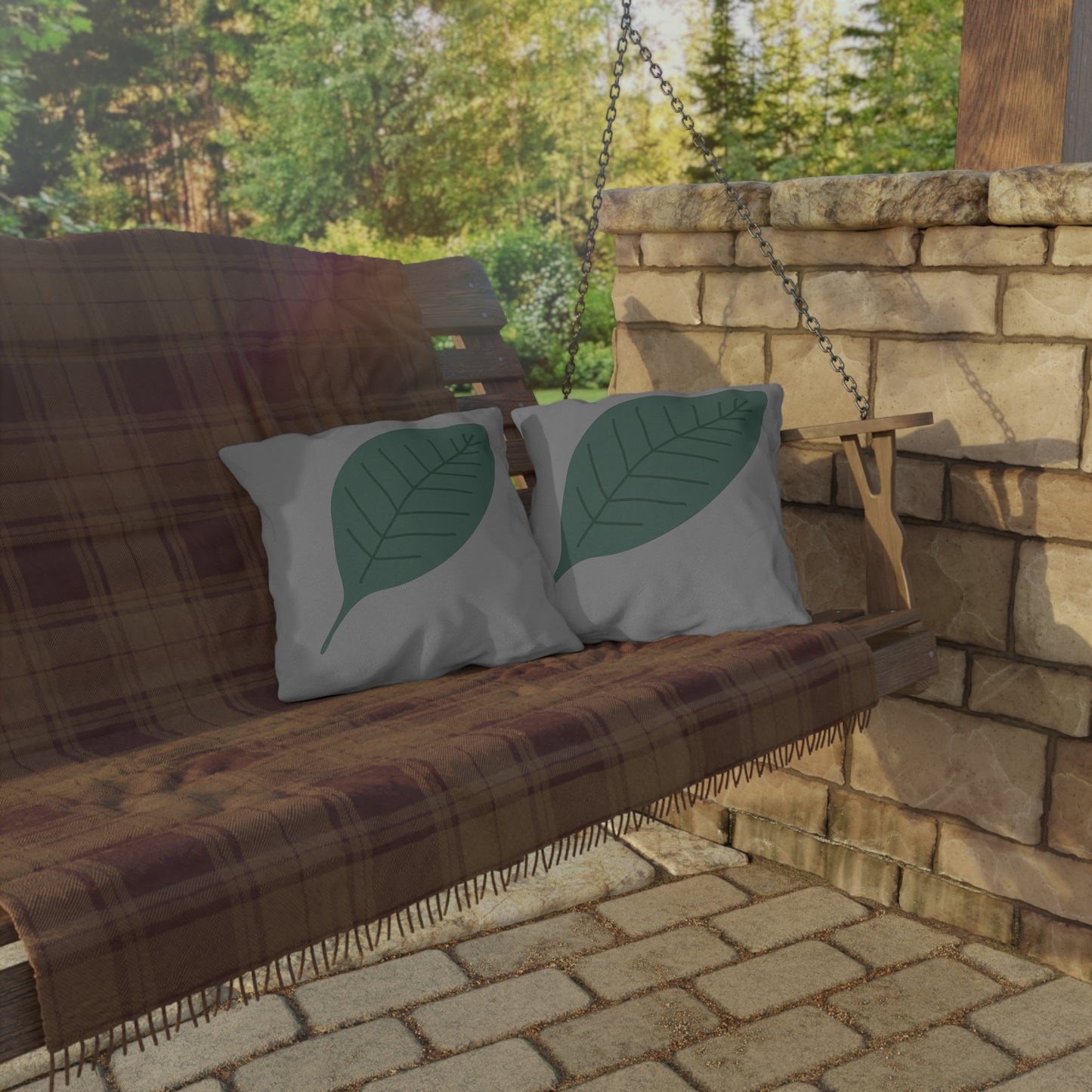 Wooden swing with plaid blanket and leaf-patterned pillows on a stone patio.