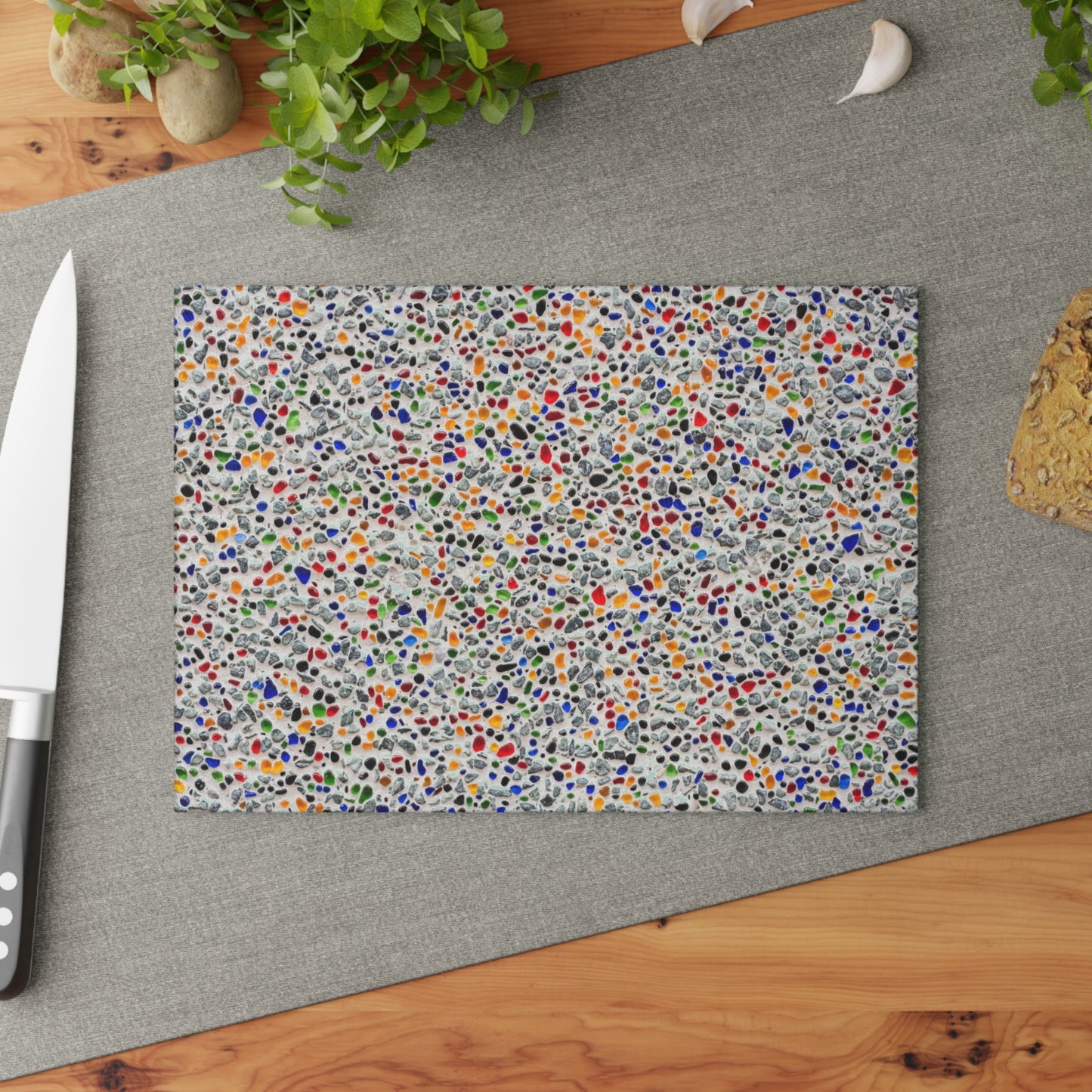 Colorful speckled cutting board on a gray surface with a knife and plant in the background.