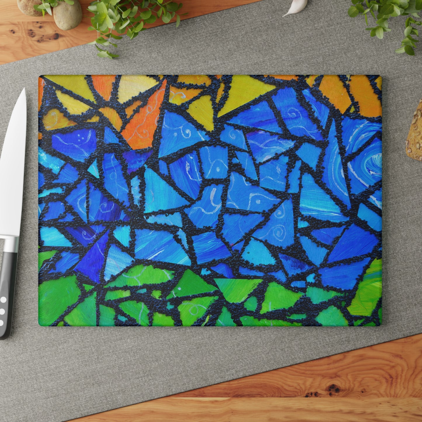 Colorful mosaic cutting board on a gray surface with a knife and plant in the background