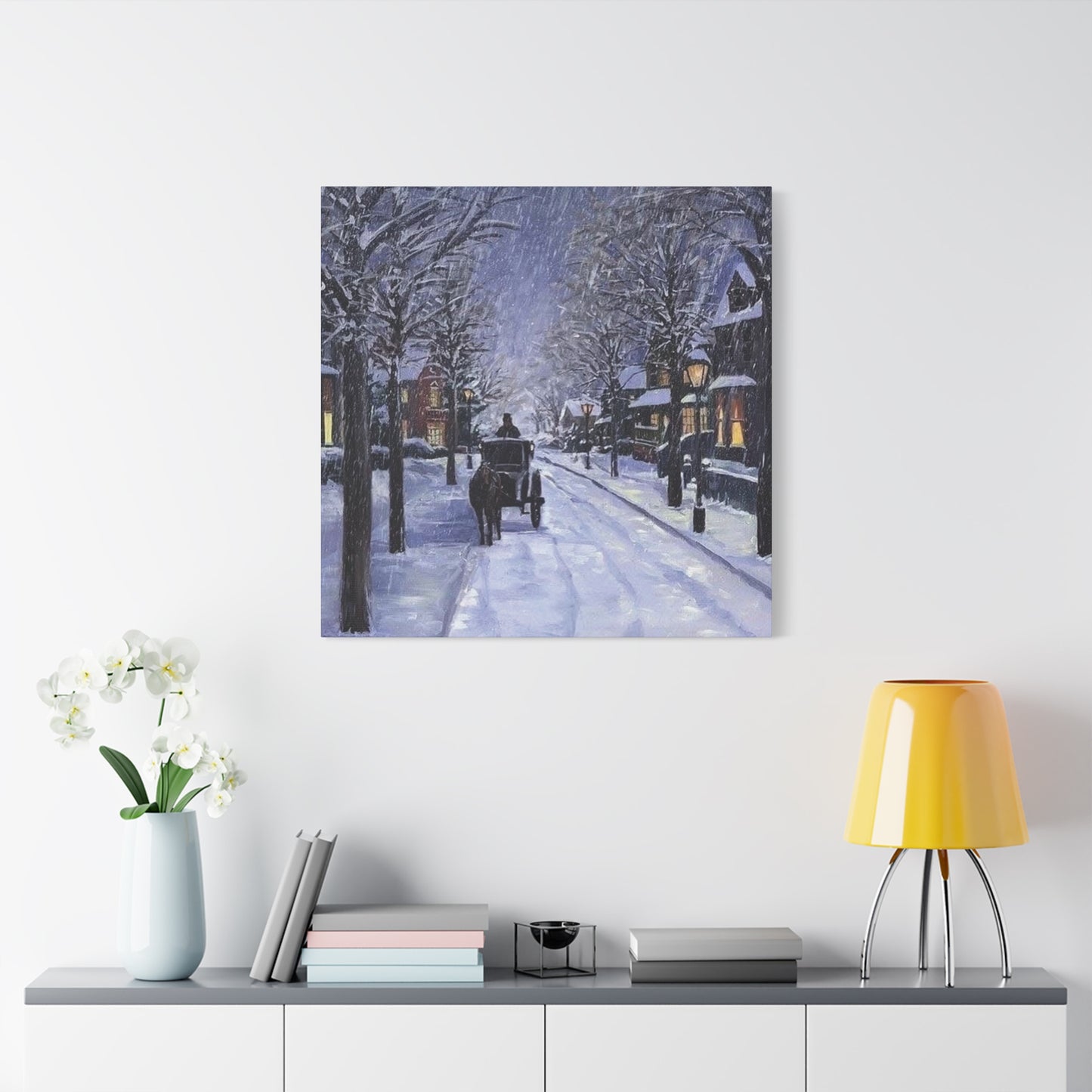 Framed artwork of a snowy street scene with a horse-drawn carriage on a white wall above a shelf.