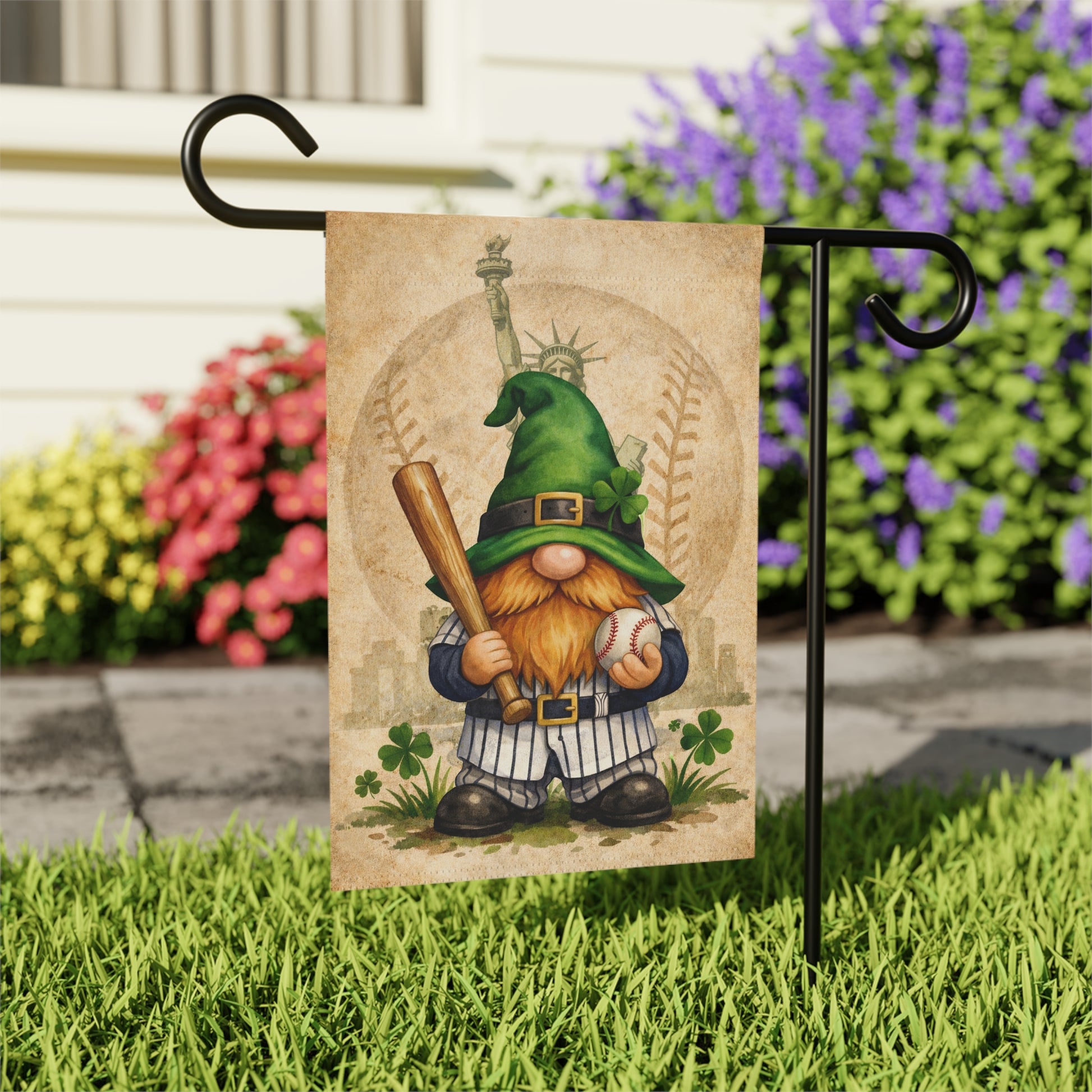 Gnome garden flag with baseball bat and ball, featuring the Statue of Liberty, on a grassy area with flowers in the background.