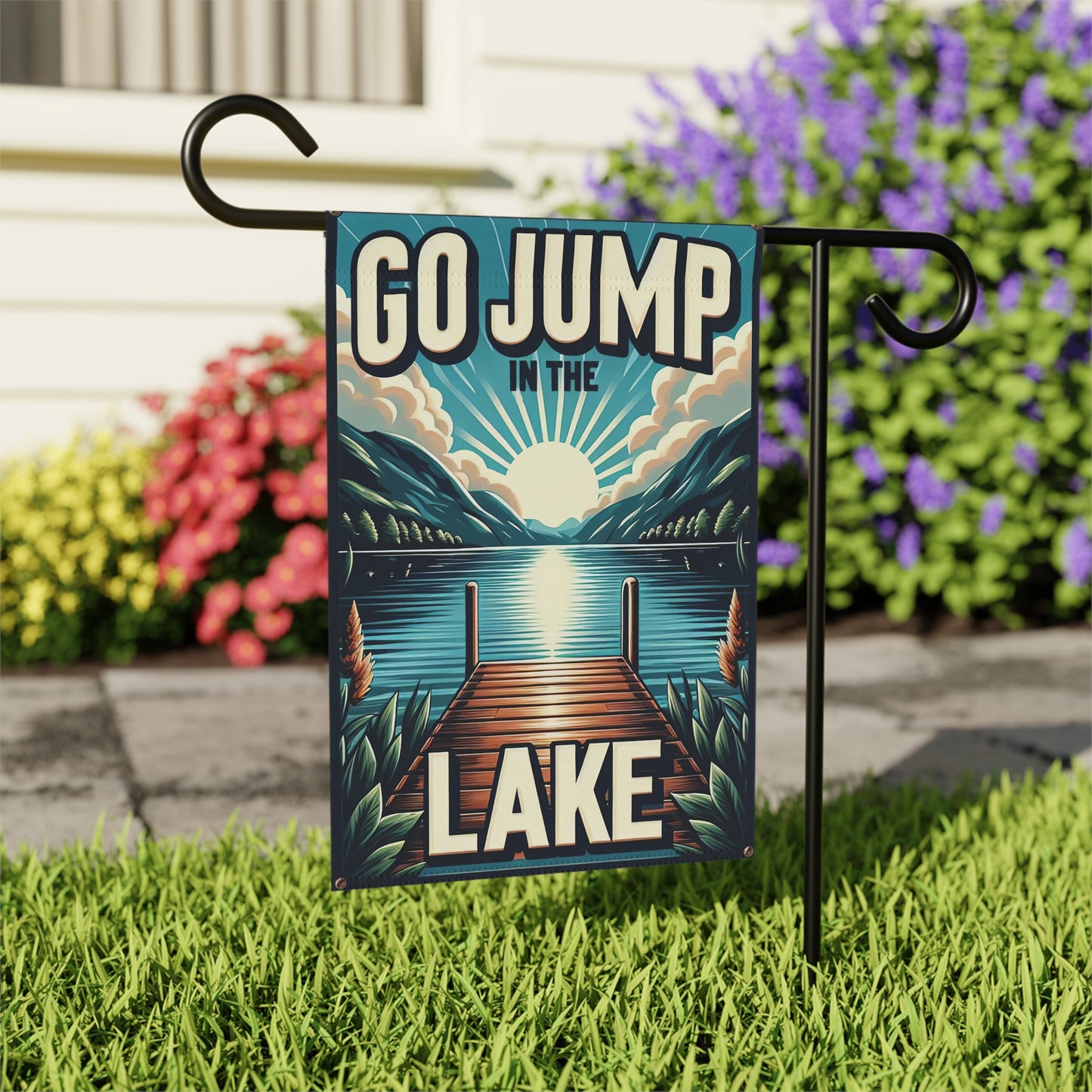 Decorative garden flag with 'Go Jump in the Lake' text and a lake scene, attached to a stand outdoors.