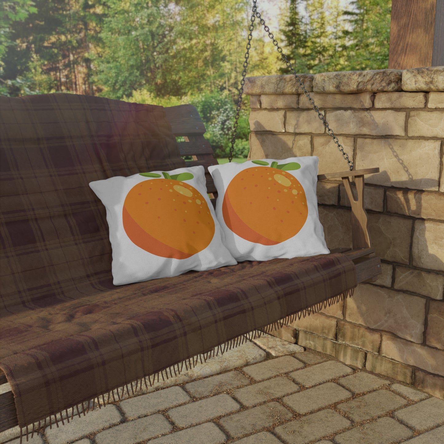 Two pillows with orange designs on a wooden swing set against a stone wall and greenery.