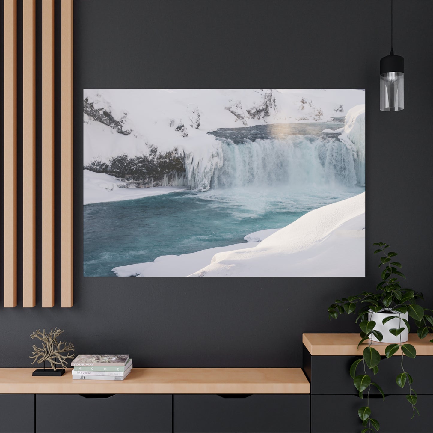 Framed photograph of a snowy landscape with a waterfall on a dark wall above a wooden shelf.