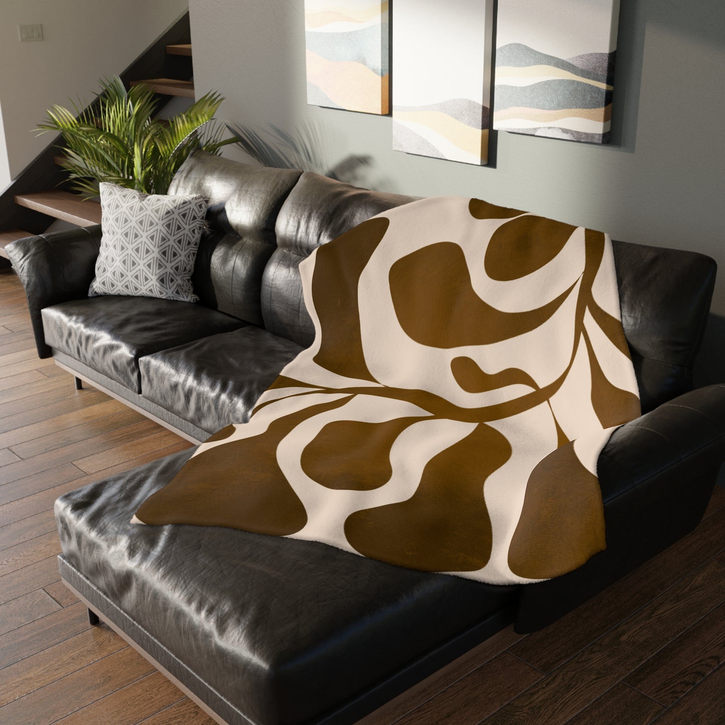 Brown and beige patterned blanket draped over a black leather sofa in a living room.
