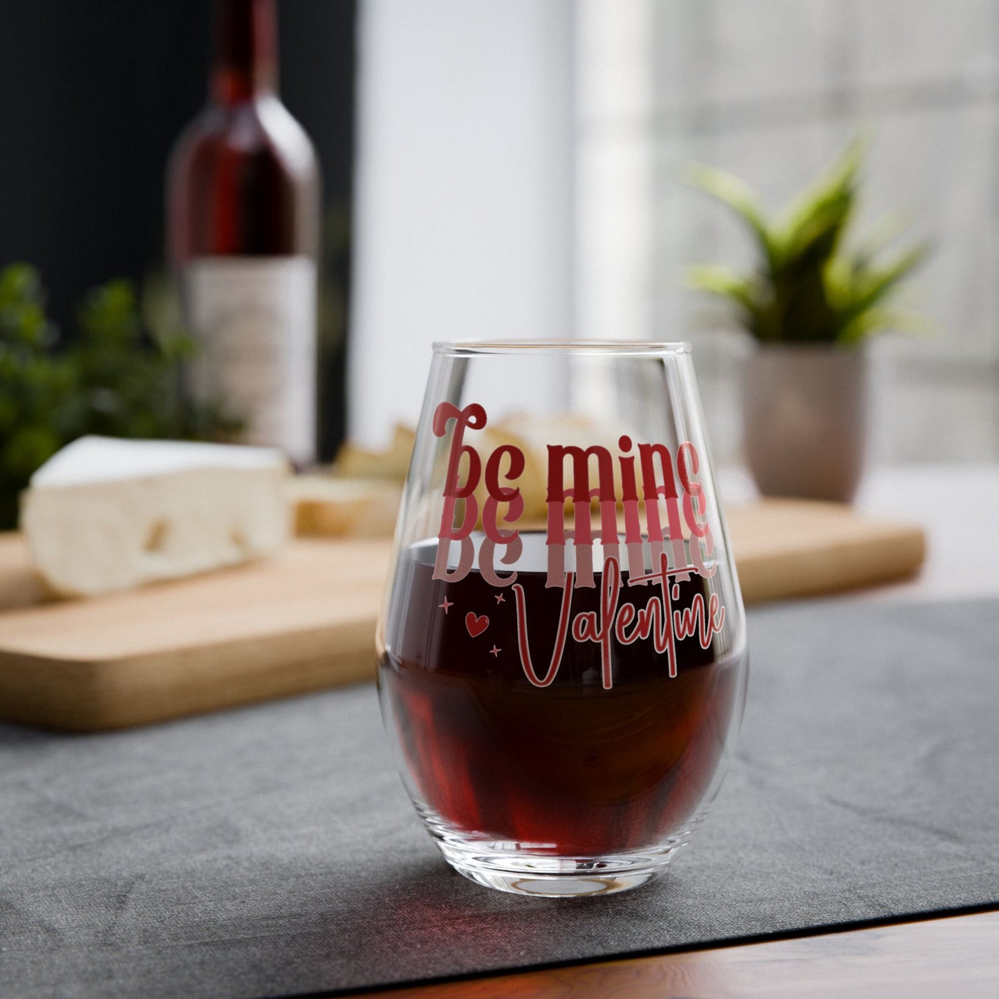 Glass with 'Be mine Valentine' text filled with red wine on a table.