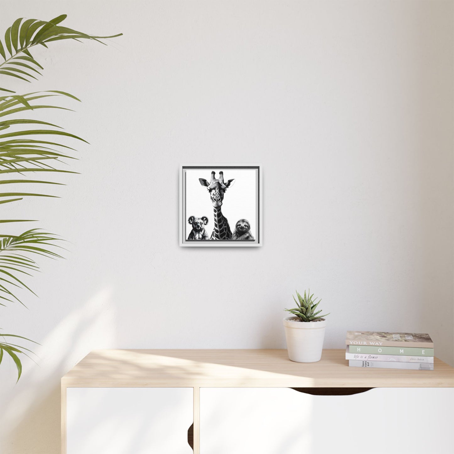 Framed artwork of a giraffe with two children on a wall above a desk with a plant and books.