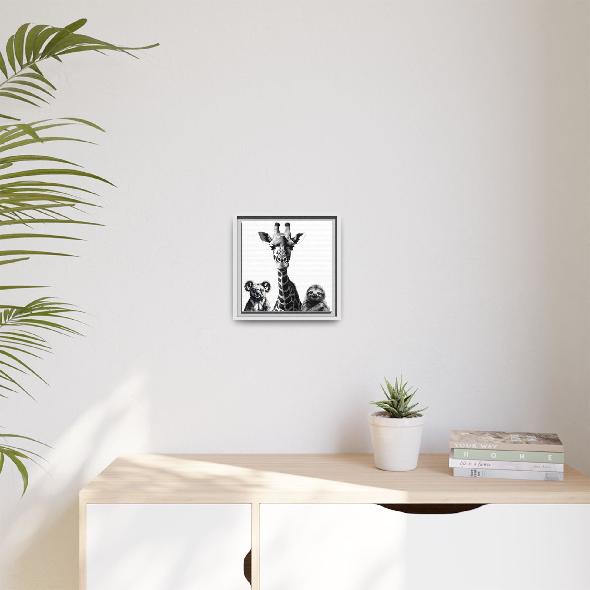Framed artwork of a giraffe with two children on a wall above a desk with a plant and books.