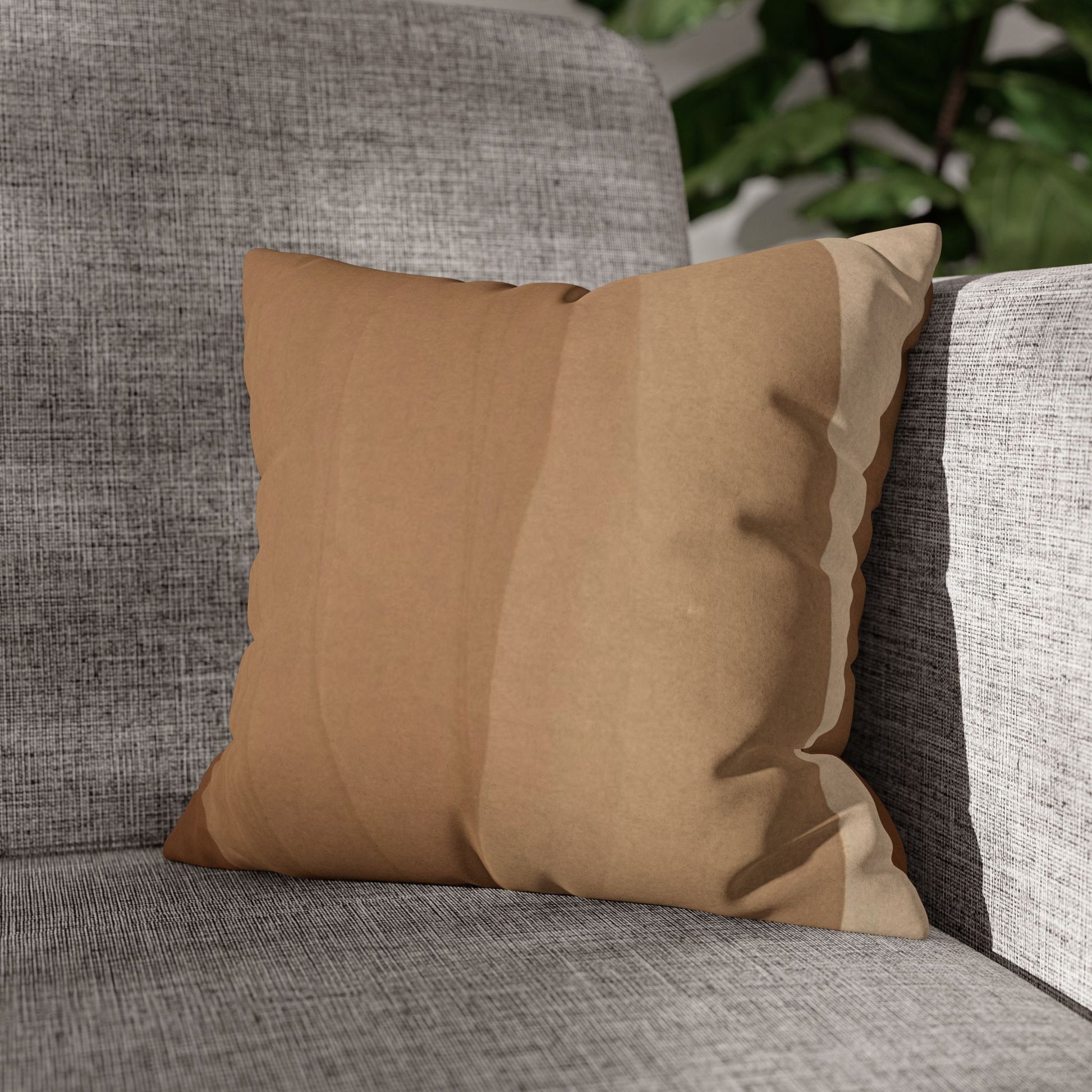Brown pillow on a gray textured sofa with greenery in the background