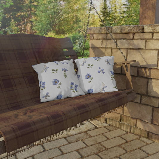 Wooden swing with plaid cover and floral pillows against a stone wall and greenery background