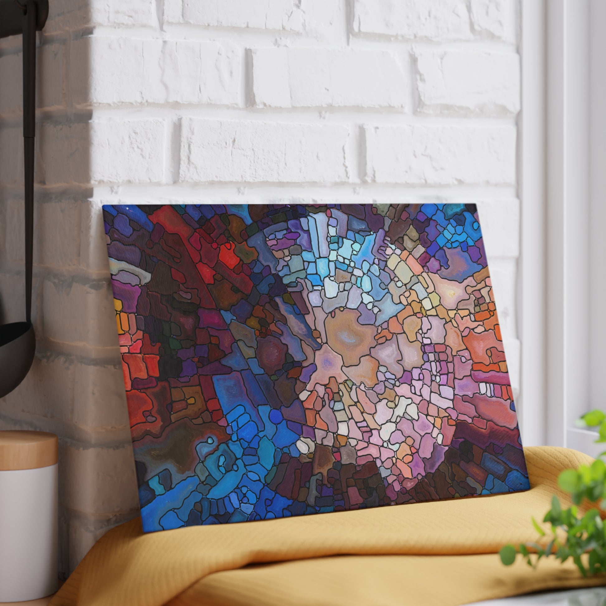 Colorful abstract painting on a white brick wall with a yellow cushion and plant in the foreground.