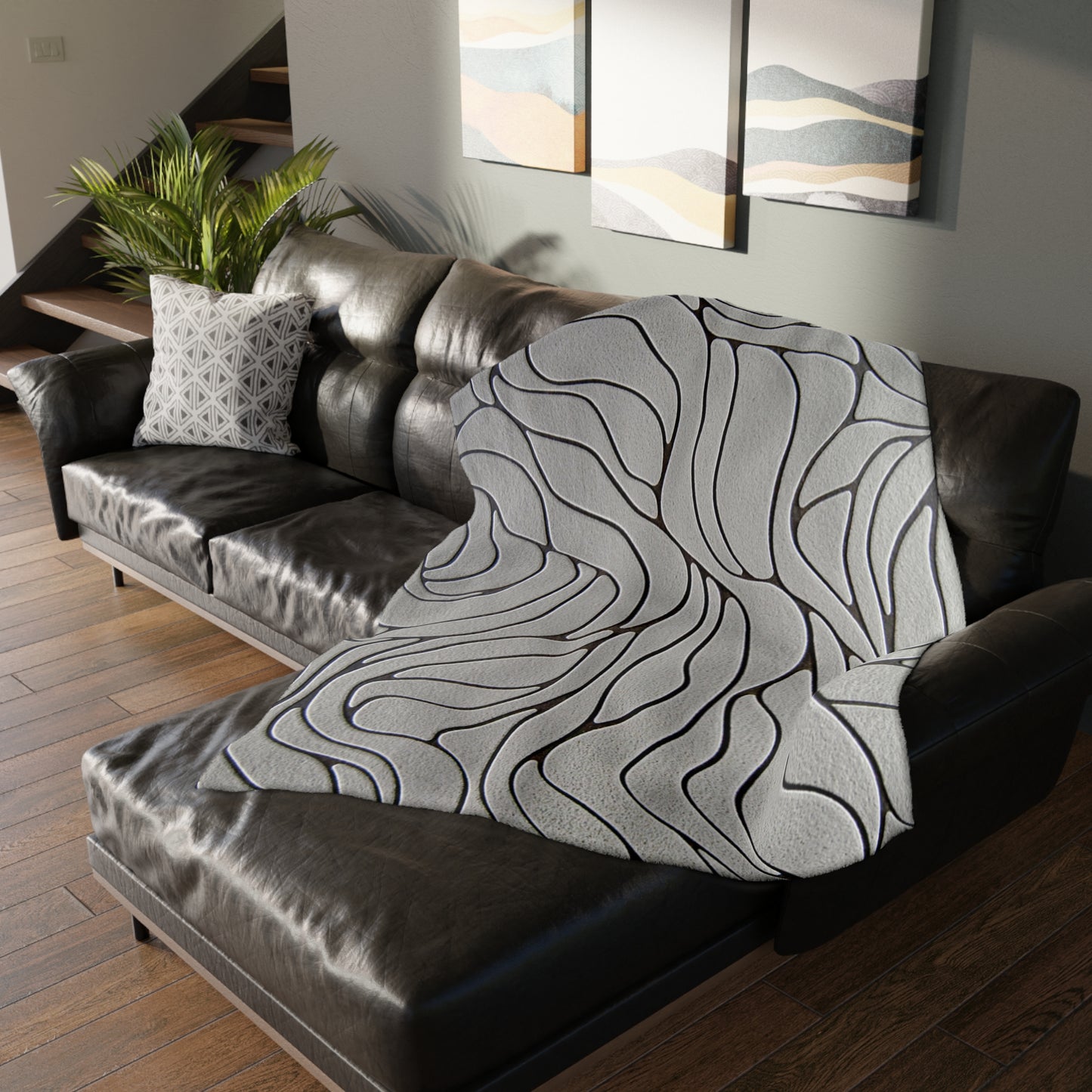 Gray patterned throw blanket draped over a brown leather sofa in a living room.