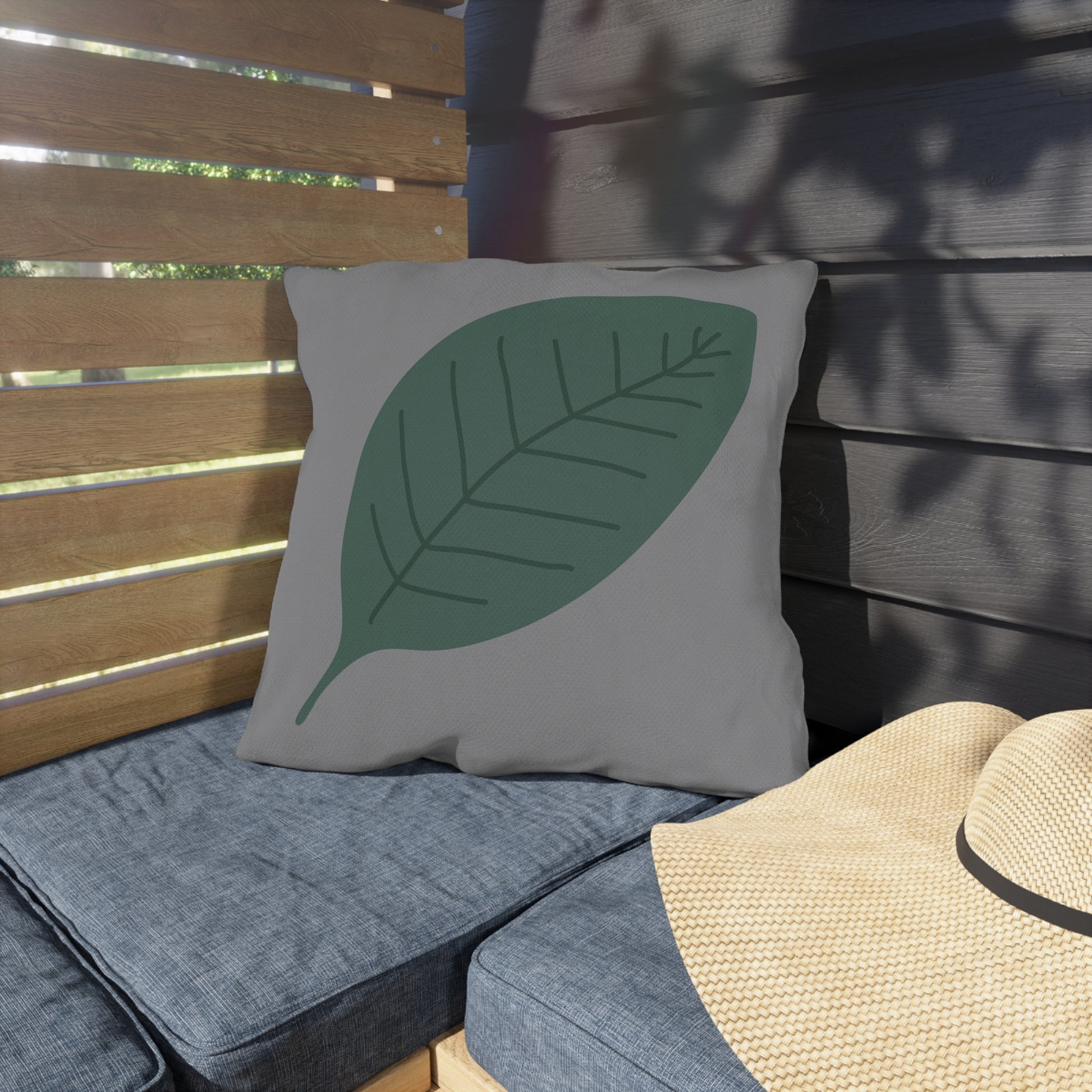 Gray pillow with a green leaf design on a wooden bench