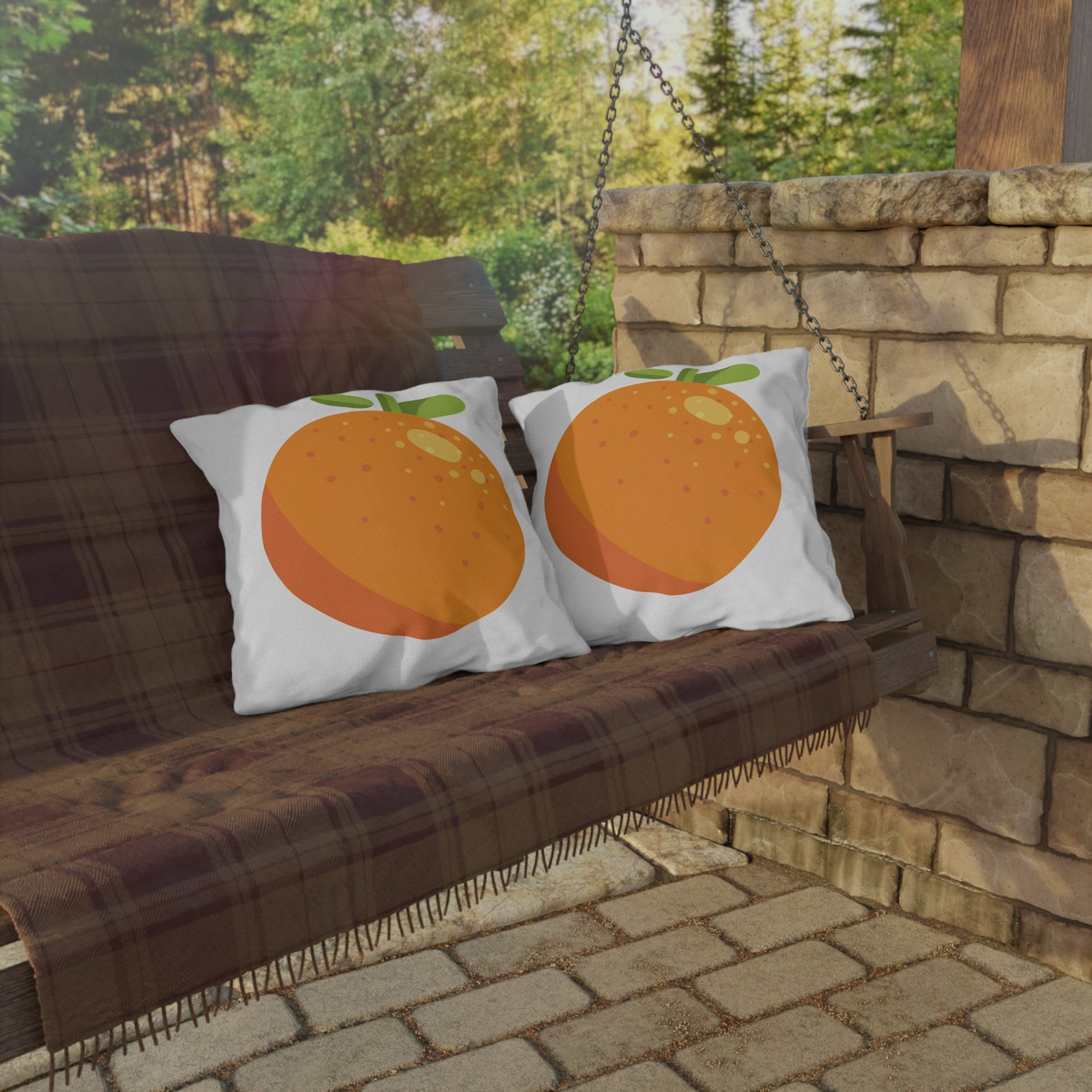 Two pillows with orange designs on a wooden swing against a stone wall and greenery background.
