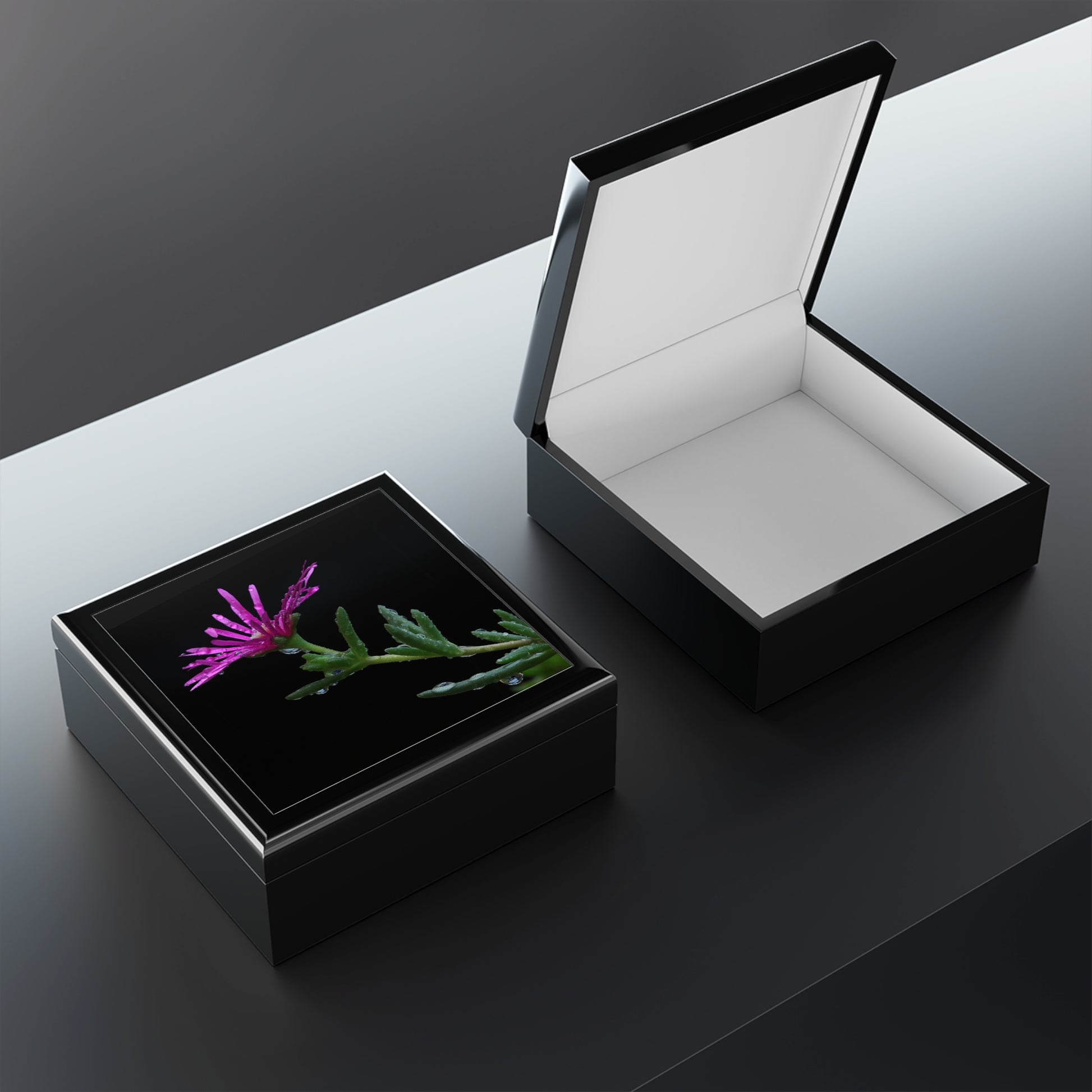 Black jewelry box with a pink flower and green leaves on a reflective surface