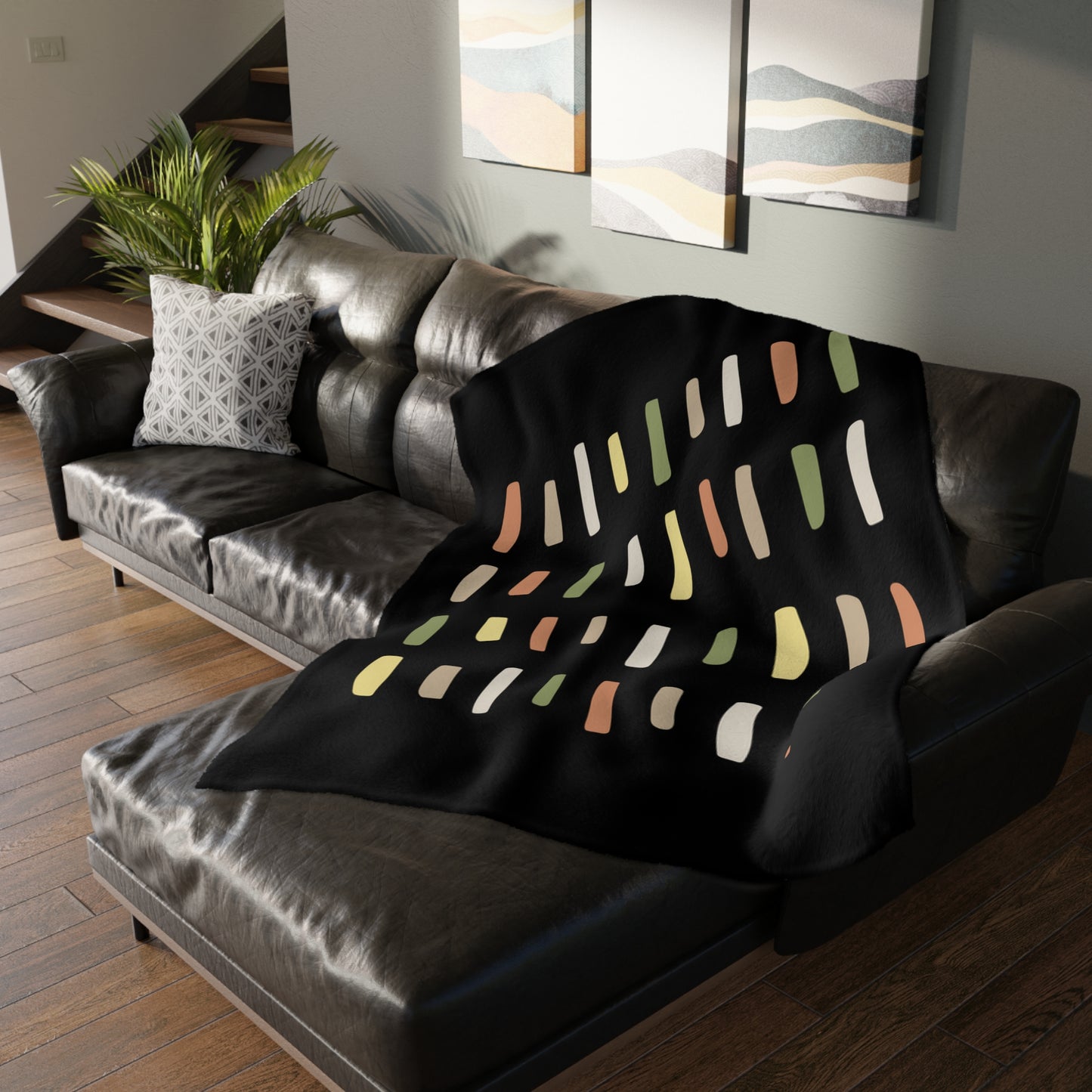 Black blanket with colorful abstract pattern draped over a gray sofa in a living room.