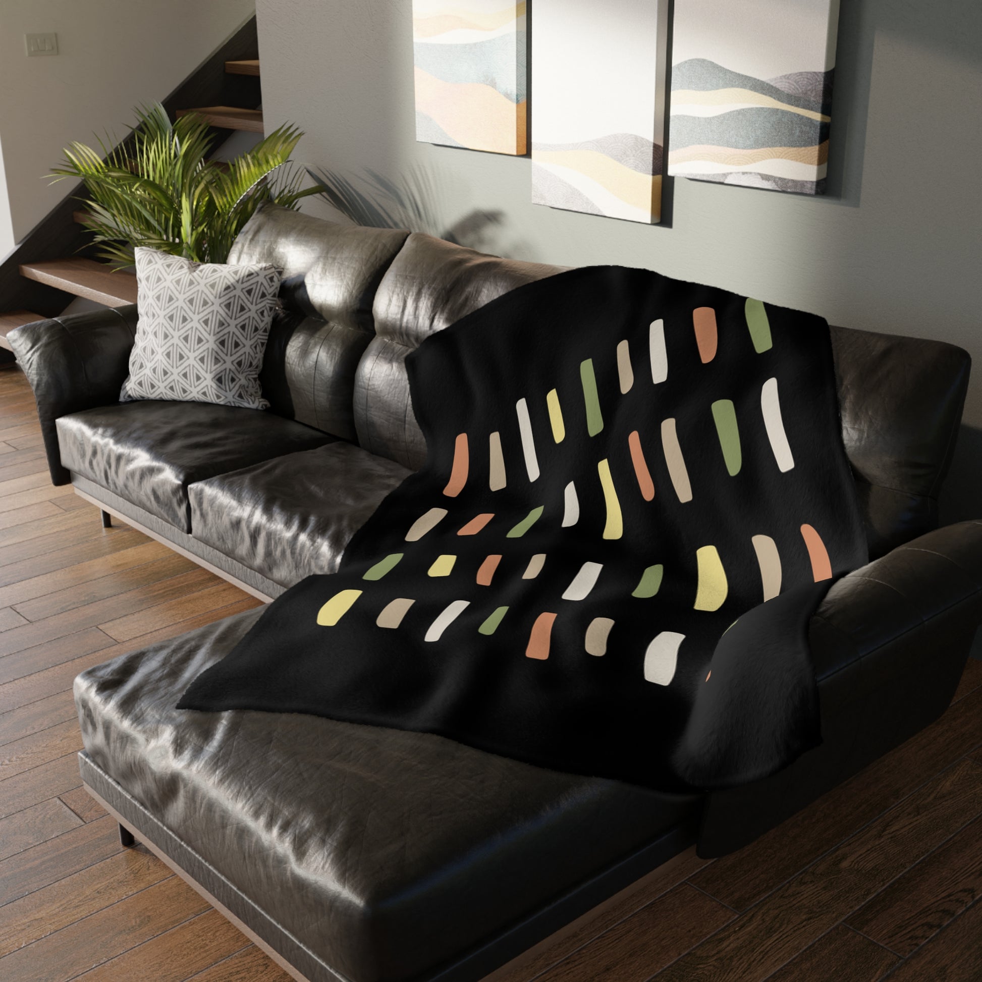 Black blanket with colorful abstract pattern draped over a gray sofa in a living room.