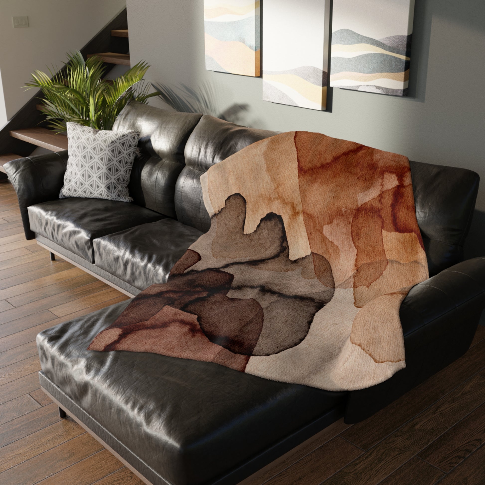 Brown patterned blanket draped over a black leather sofa in a living room.