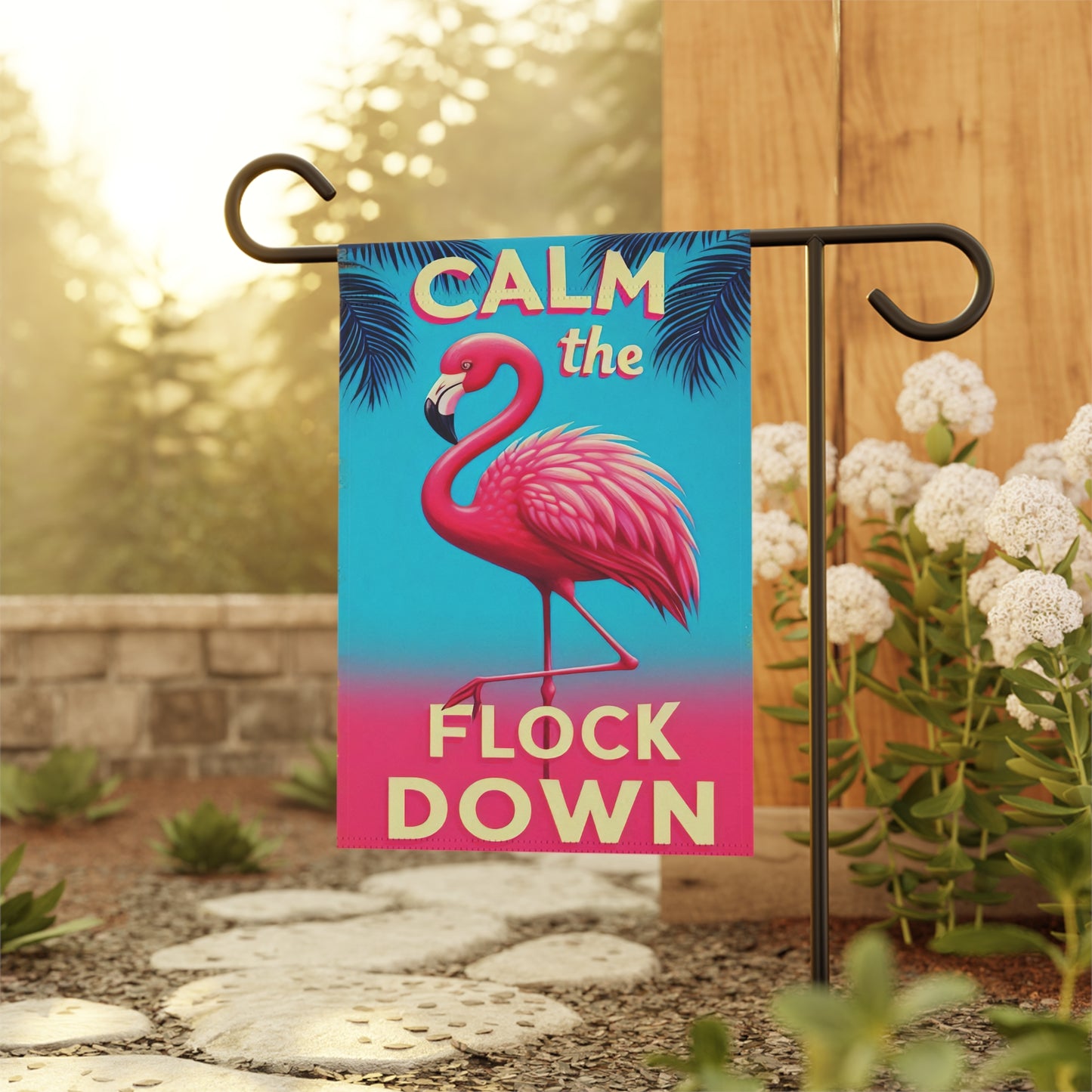 Garden flag with a flamingo design and text 'Calm the Flock Down' on a stand outdoors.