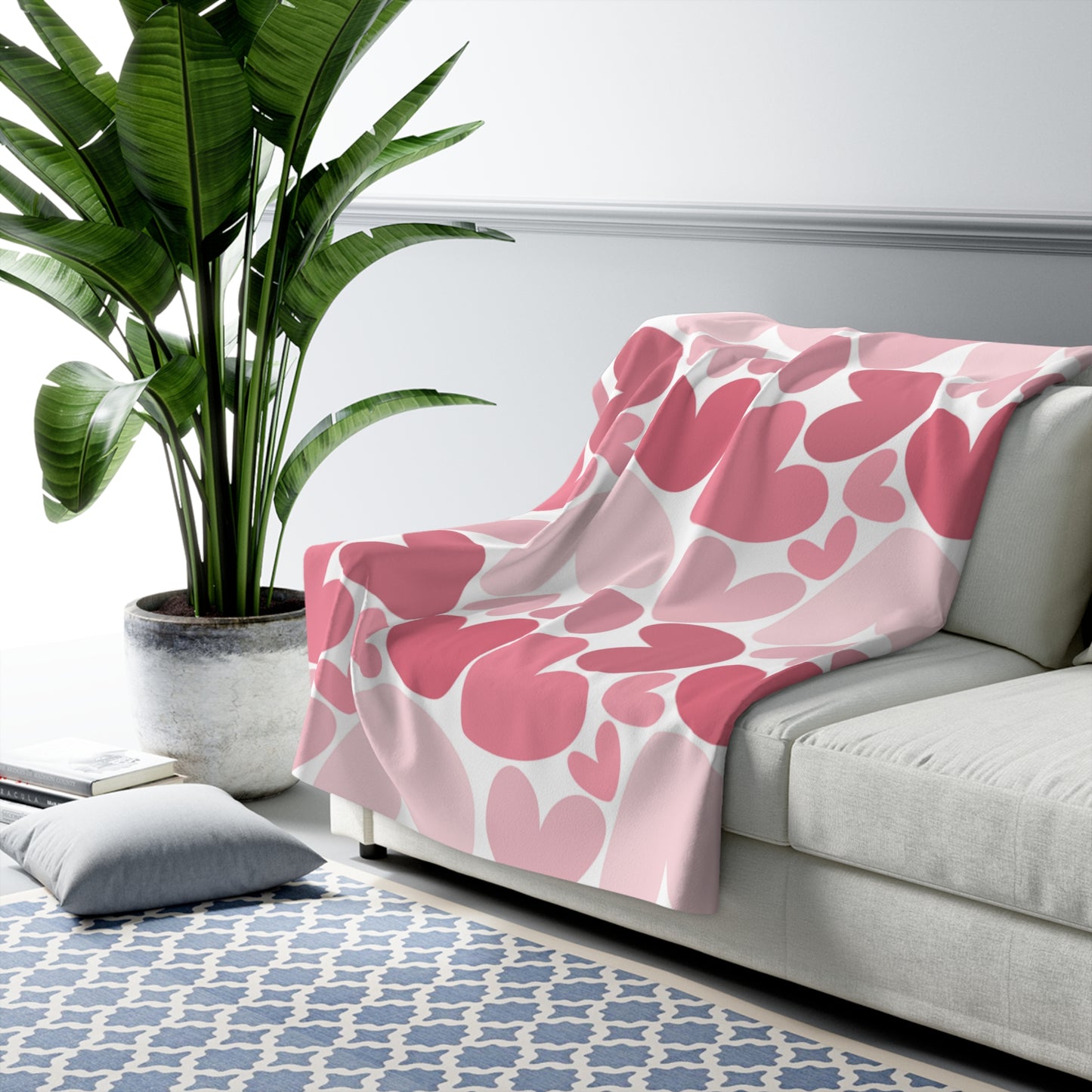 Pink floral blanket on a gray sofa with a plant and rug in the background