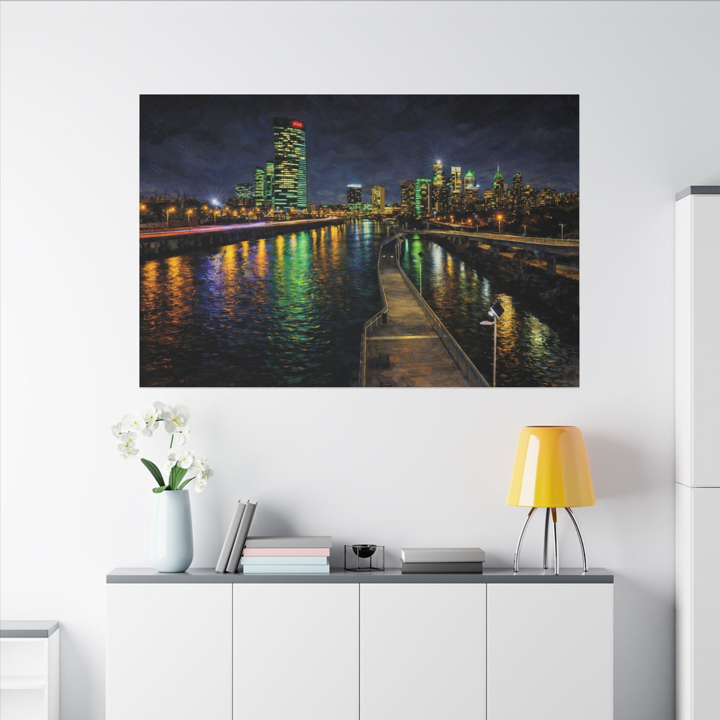 Cityscape at night with illuminated buildings reflected in water, displayed on a wall above a white cabinet.