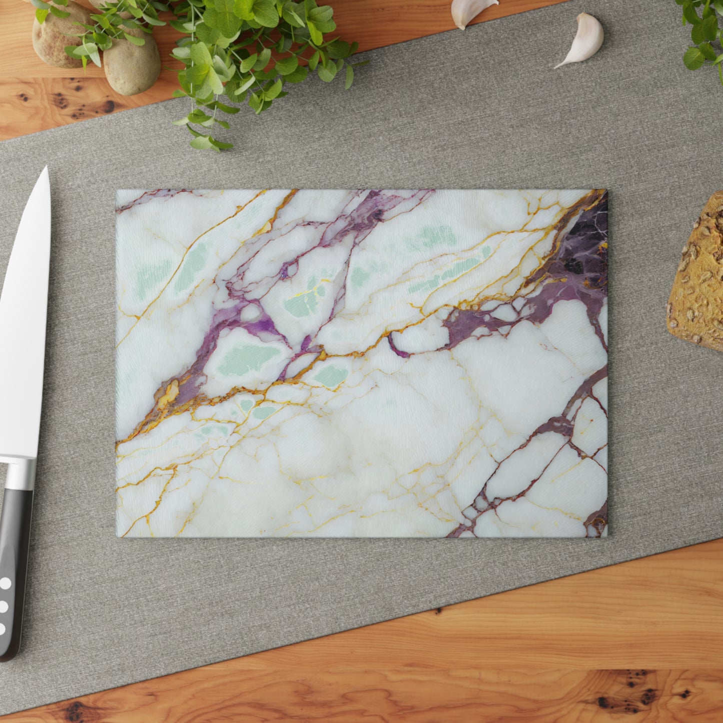 Marble-patterned cutting board on a kitchen surface with a knife and plants.