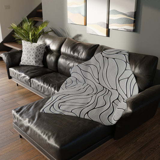 Brown leather sectional sofa with a patterned gray throw blanket in a living room setting.