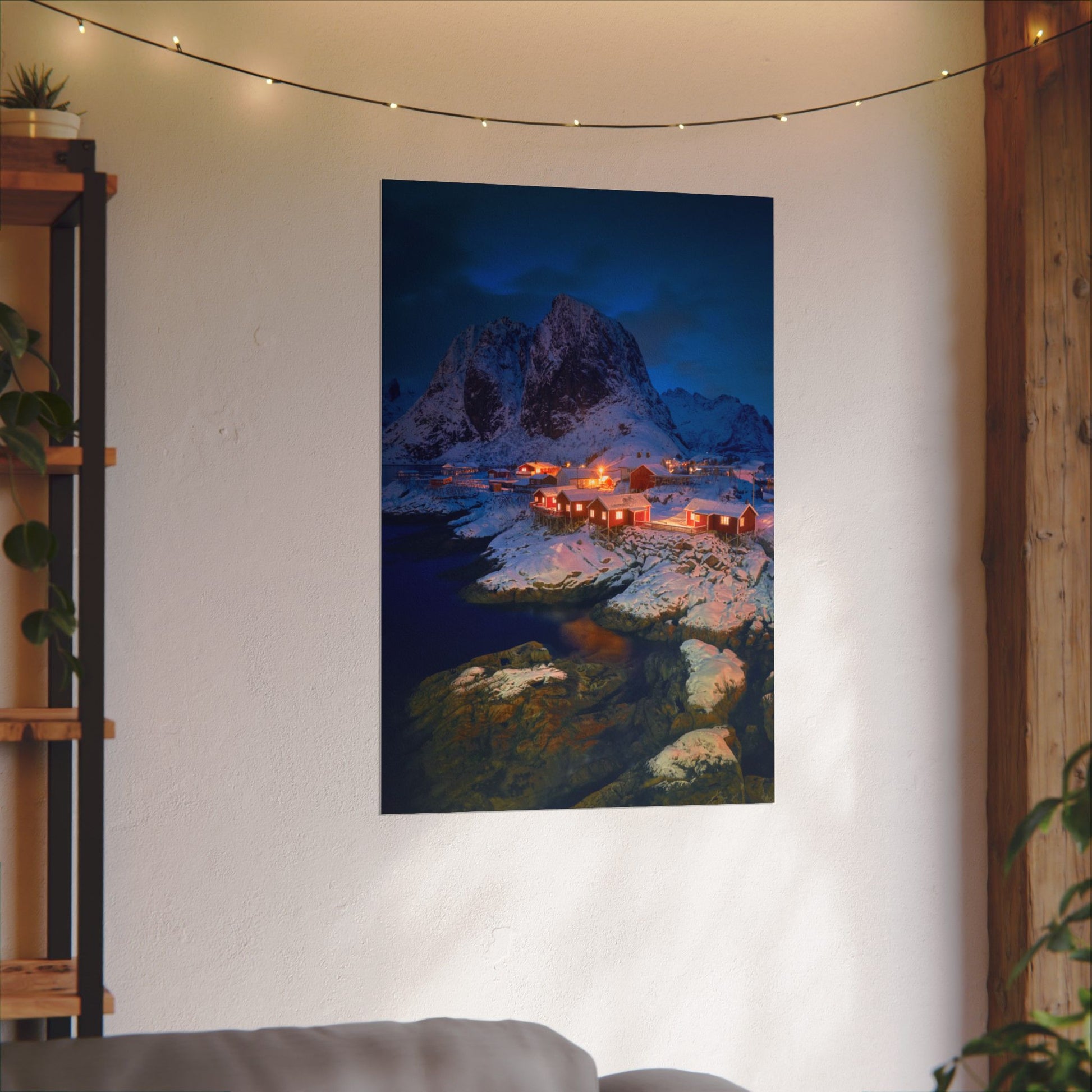 Poster of a mountain village scene hanging on a wall with string lights above.