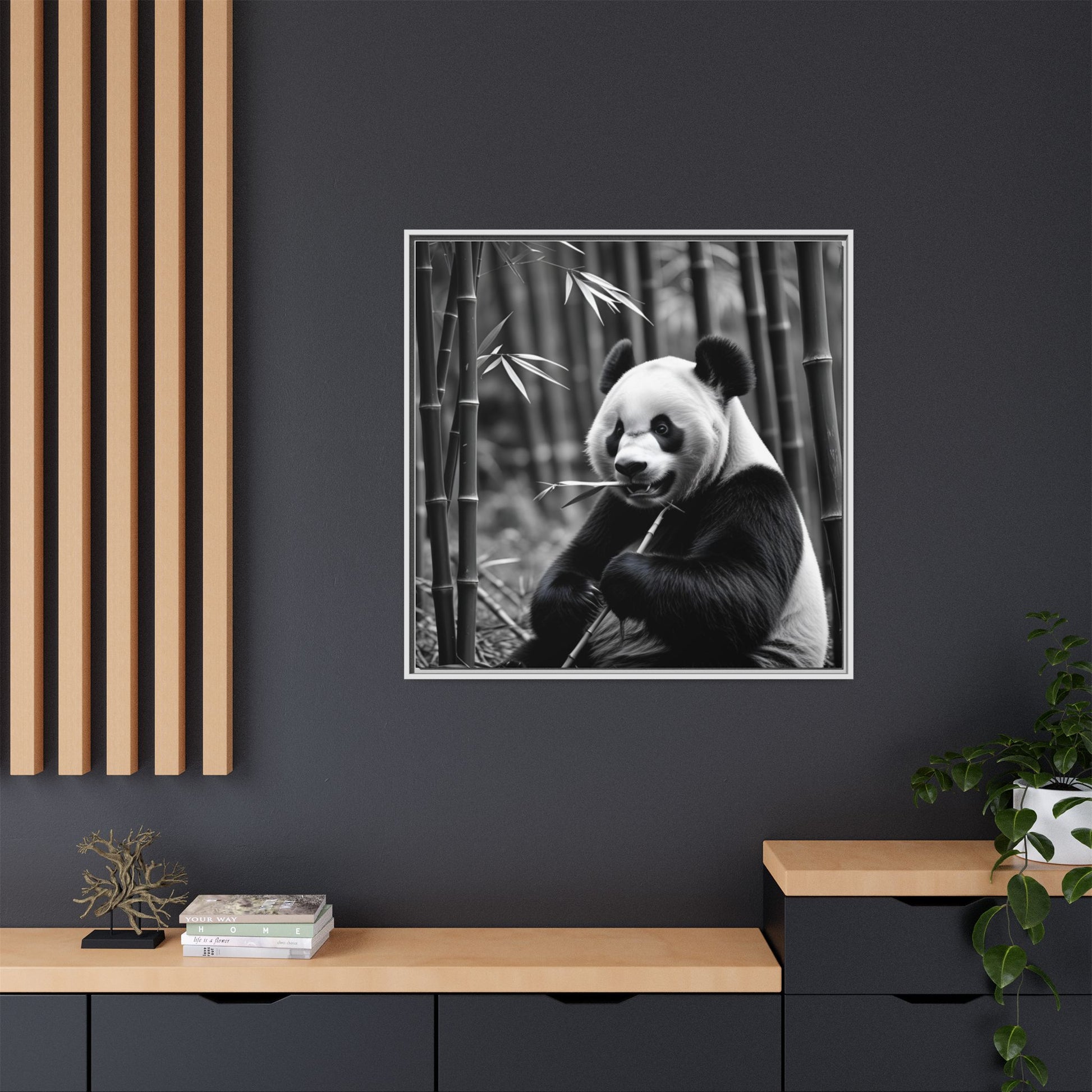 Framed black and white photo of a panda eating bamboo on a dark wall.