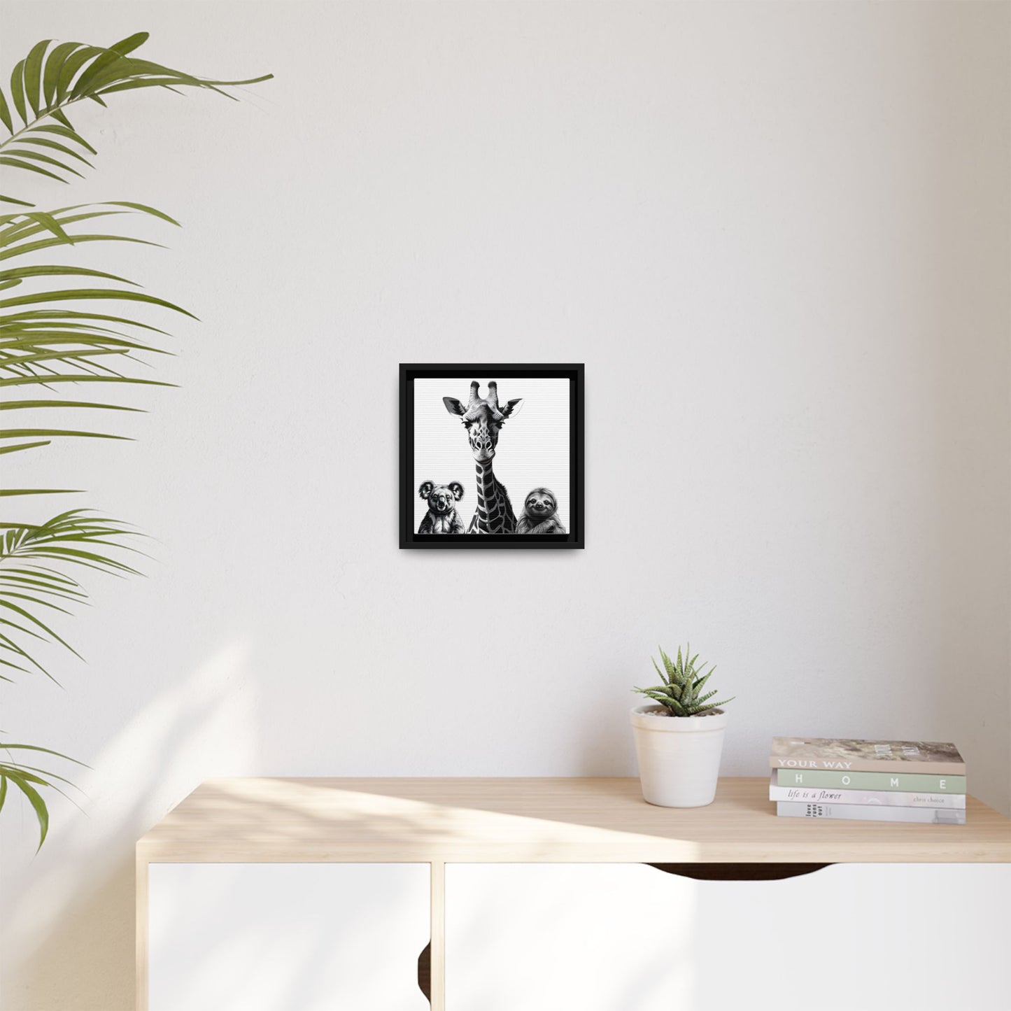 Framed artwork on a wall above a desk with a plant and books.