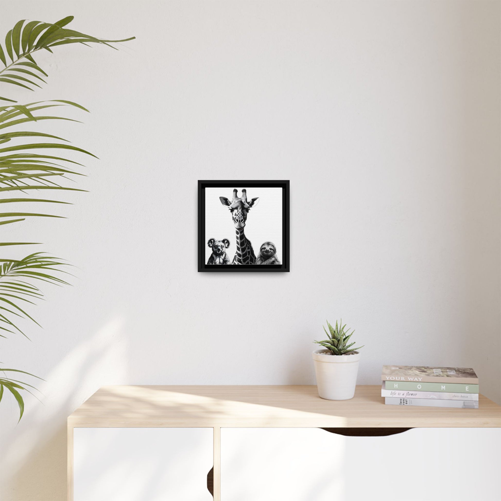 Framed artwork on a wall above a desk with a plant and books.
