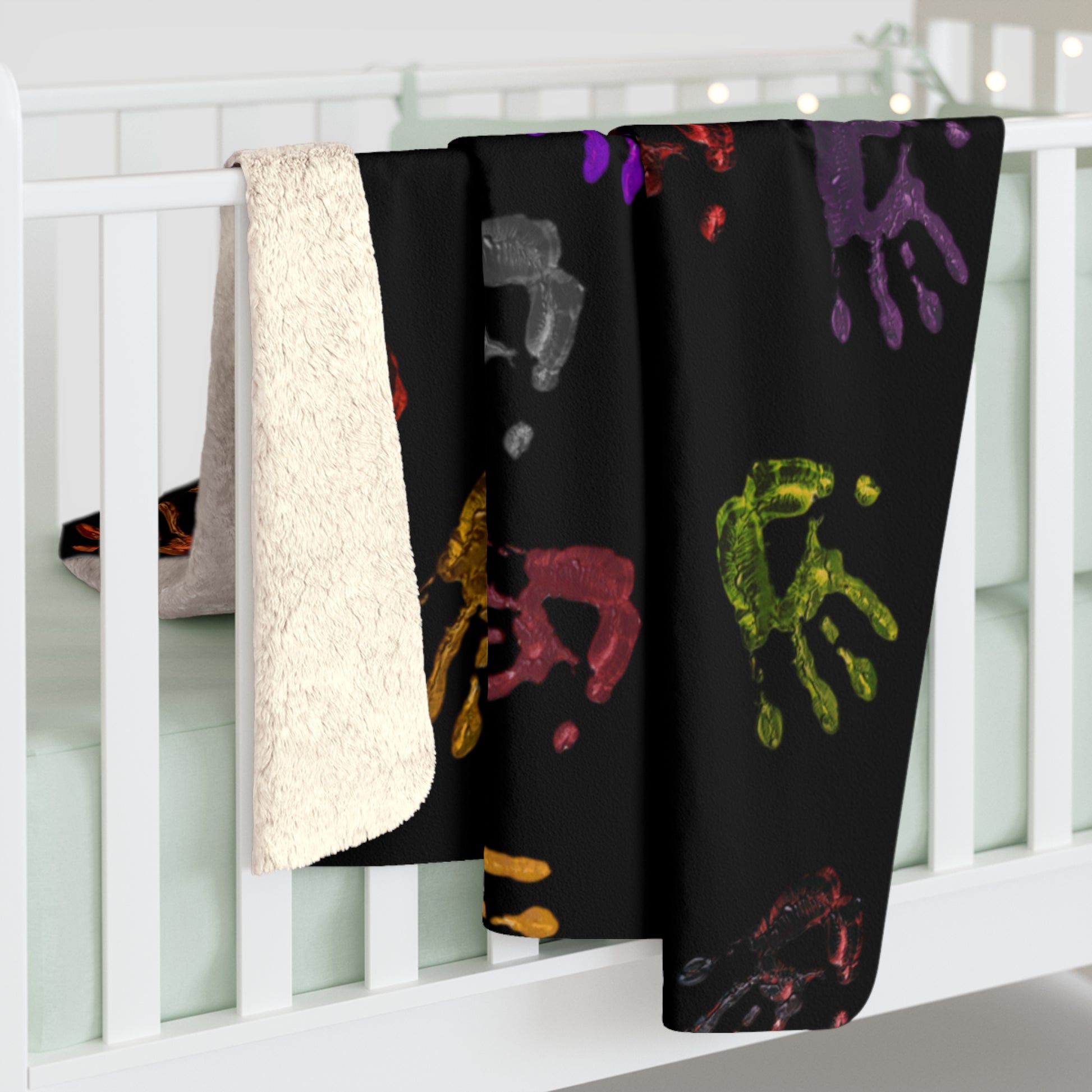 Black blanket with colorful handprints draped over a white crib
