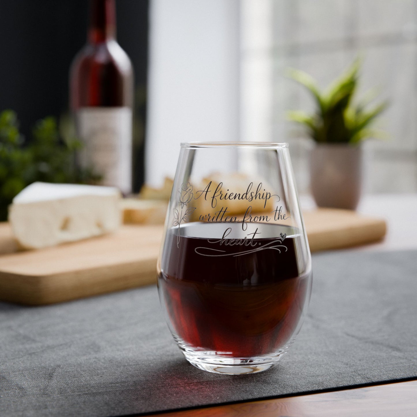 Glass of red wine with 'Friendship written from the heart' text on a table with cheese and wine bottle in the background.