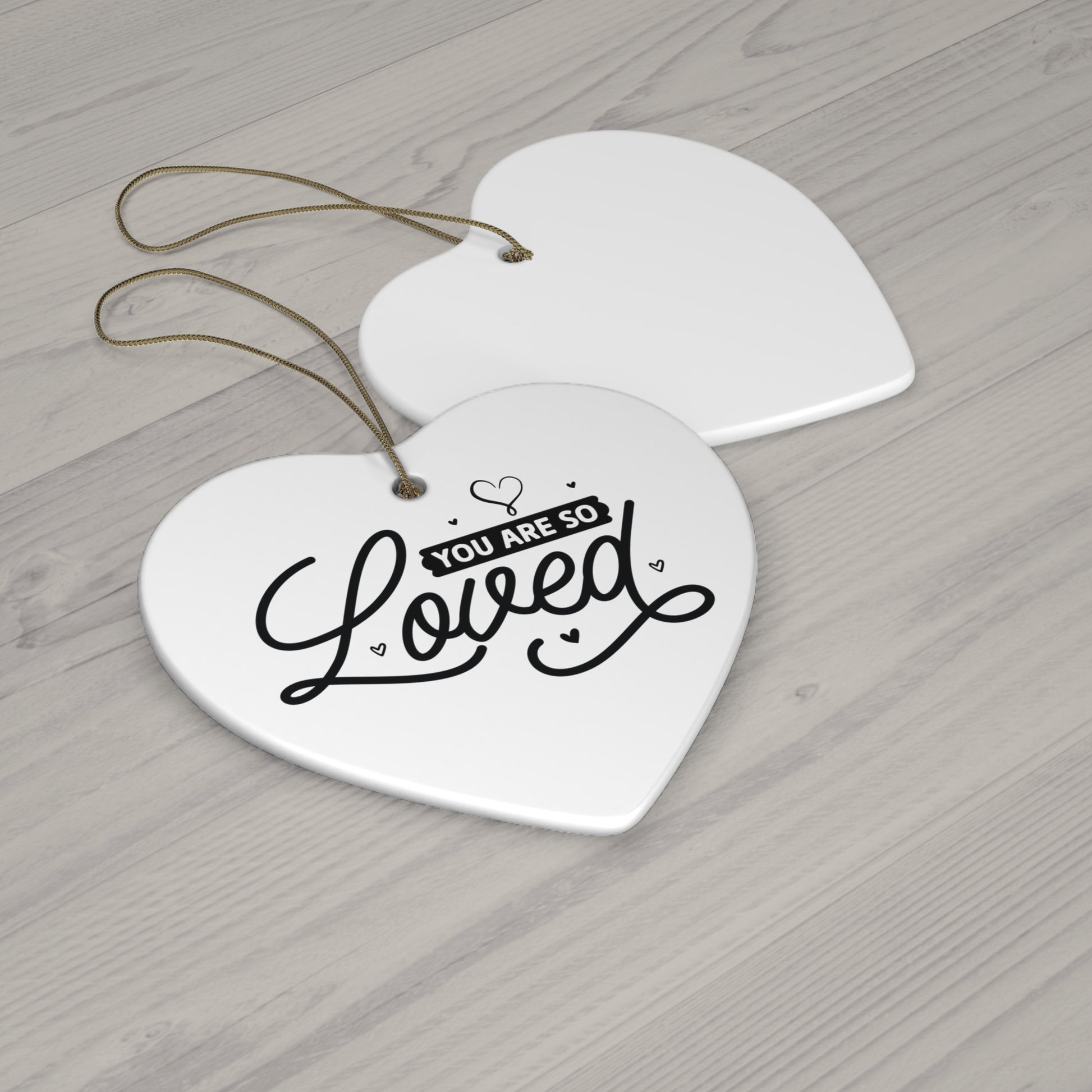 Heart-shaped ceramic tag with 'You are so loved' text on a wooden surface