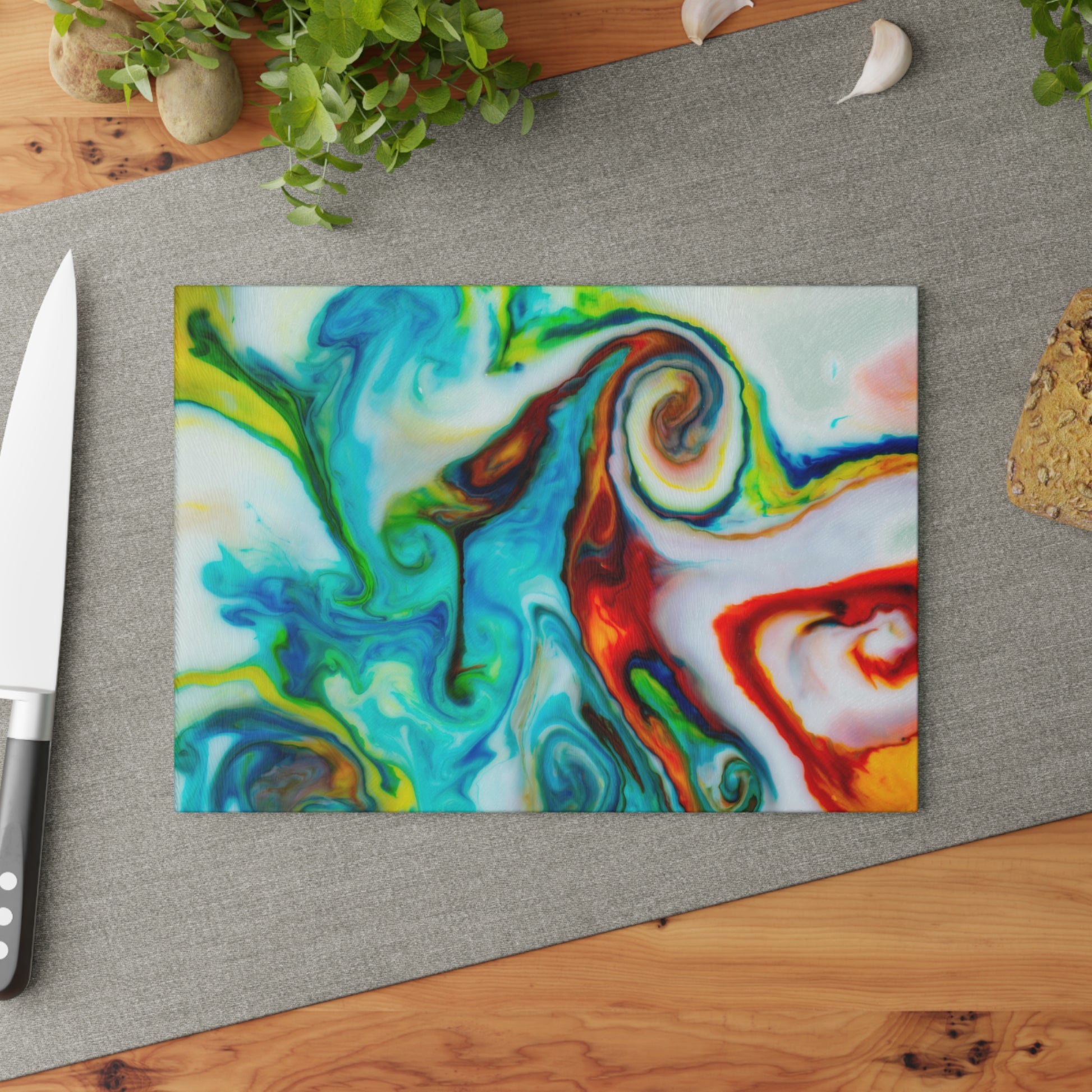 Colorful abstract design on a glass cutting board with a knife and plant in the background.