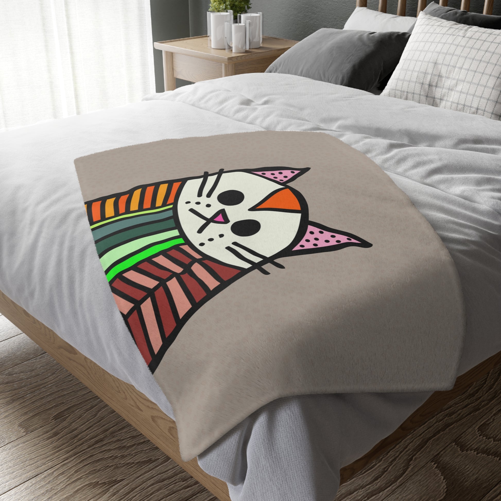 Colorful cat face design on a beige blanket over a bed.